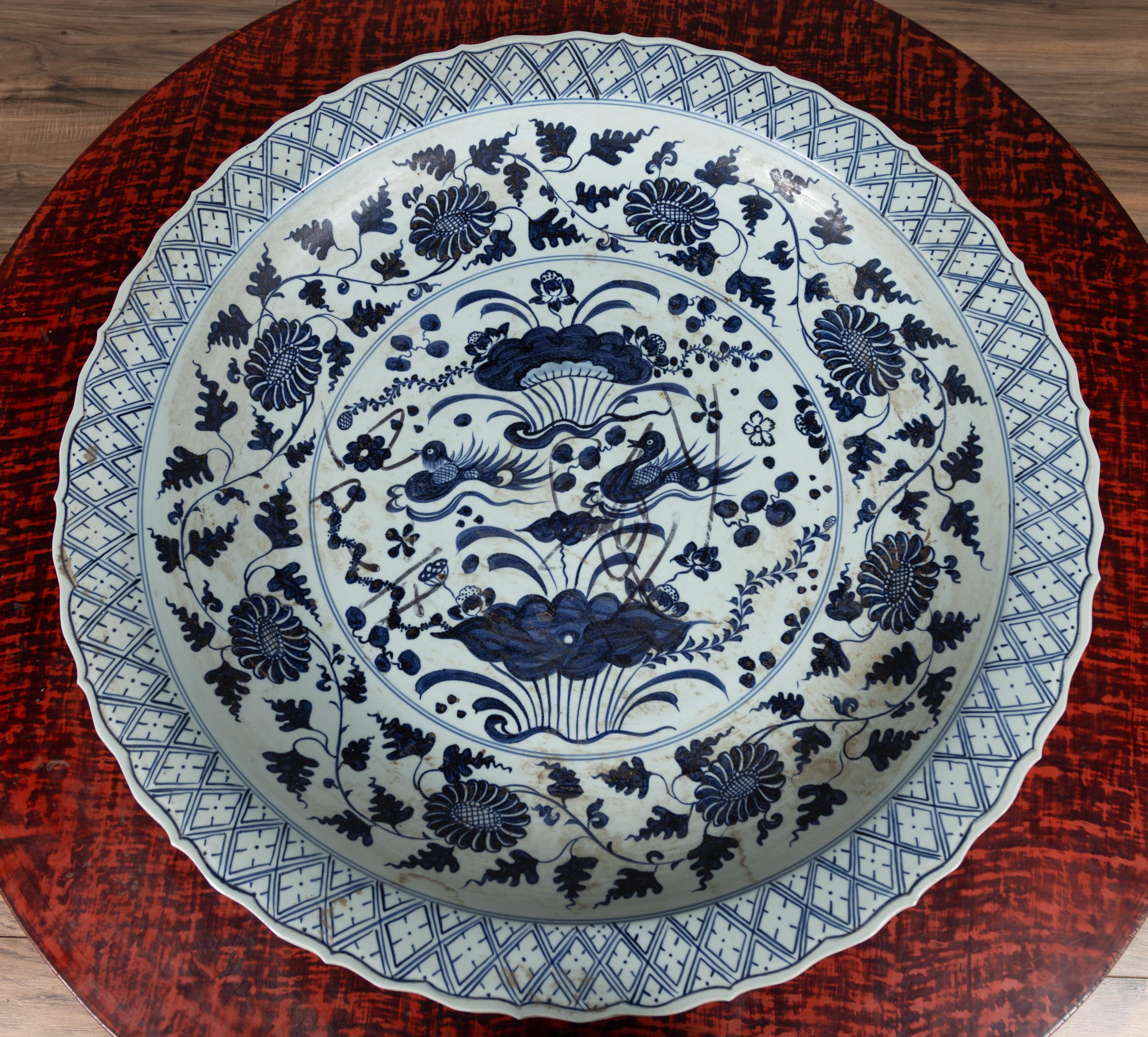 A large Chinese vintage blue and white charger plate from the 20th century, with underglaze décor of flowers and birds. Born in China, this lovely charger plate features a delicately scalloped border, adorned with a succession of X-shaped motifs,