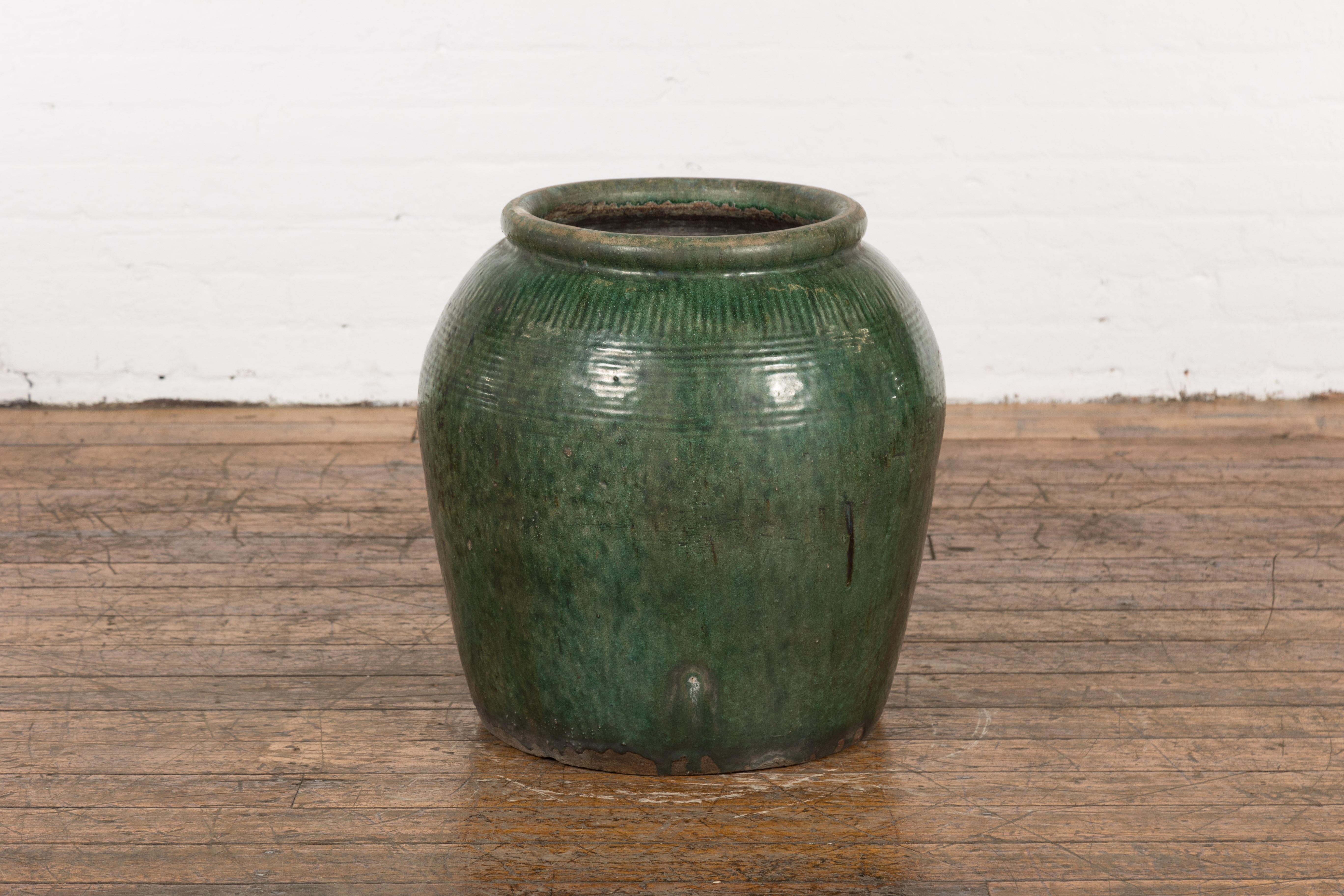 A large vintage Chinese green glazed ceramic planter from the mid 20th century with thick lip, striated décor and nicely weathered appearance. This large Chinese green glazed ceramic planter from the mid 20th century is an exquisite blend of