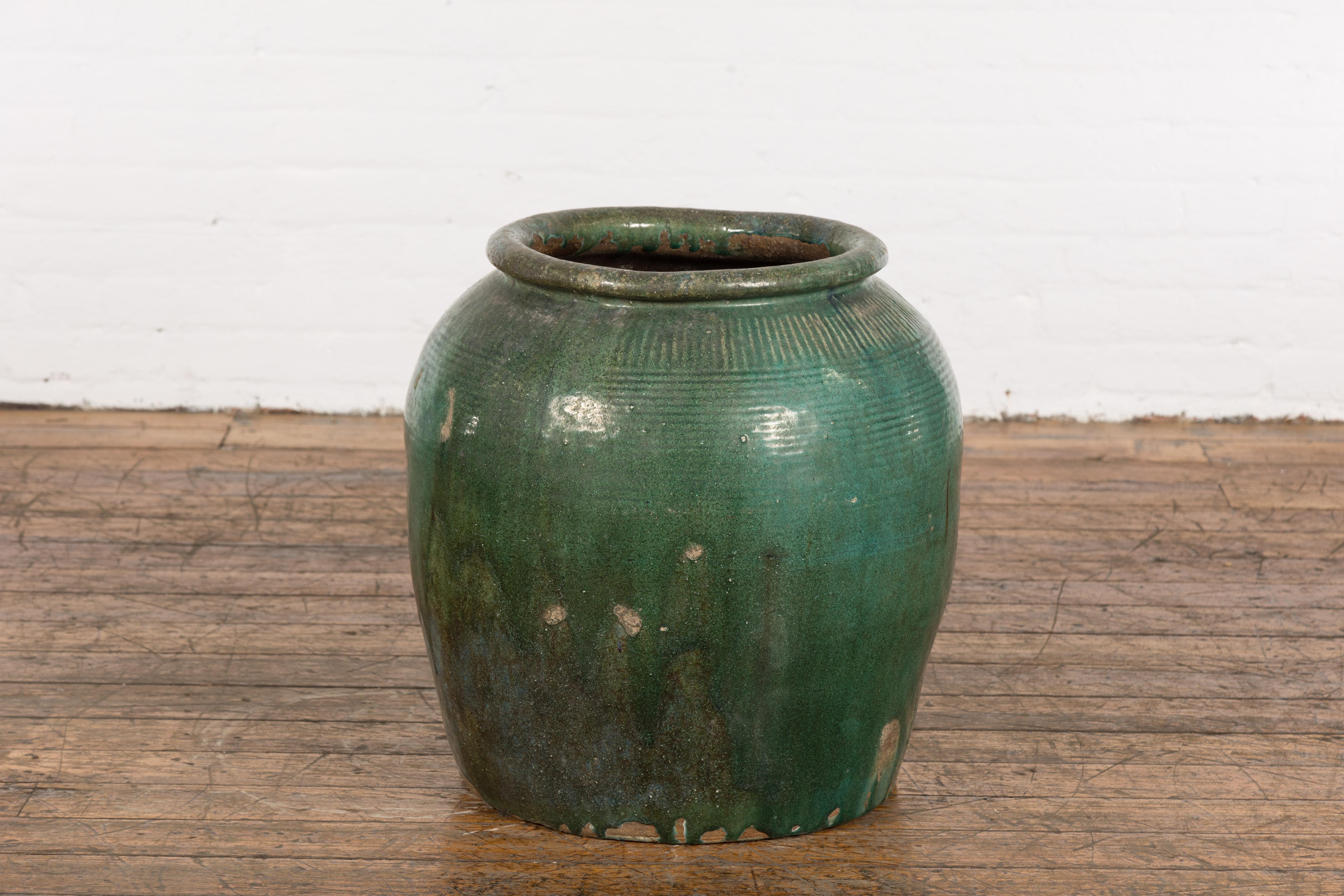A large Chinese green glazed ceramic planter from the mid 20th century with large lip, striated décor and nicely weathered appearance. Charming us with its large proportions and slightly weathered appearance revealing its age and use, this green