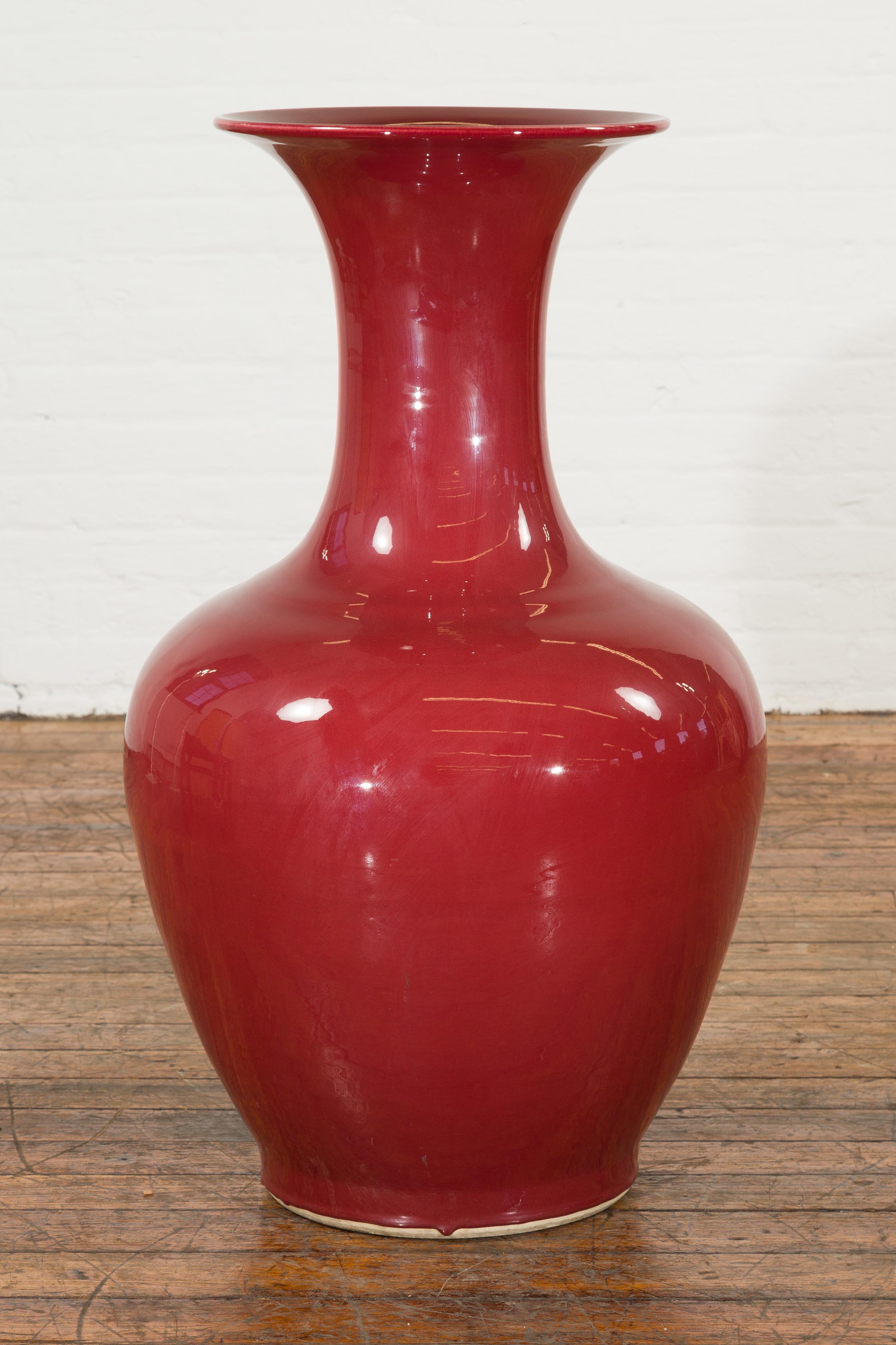 A large vintage oxblood altar vase with flaring neck. This large vintage oxblood altar vase captivates with its rich, deep finish and elegant silhouette. The vase features a gracefully flaring neck that transitions smoothly into a generous body,
