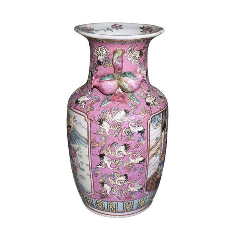 A large chinoiserie famille rose ceramic vase with a lovely floral, figural, and bird motif. This polychrome vessel is wide at the body, and narrow at the neck and base. It has a bright pink background and is decorated with multiple white flying