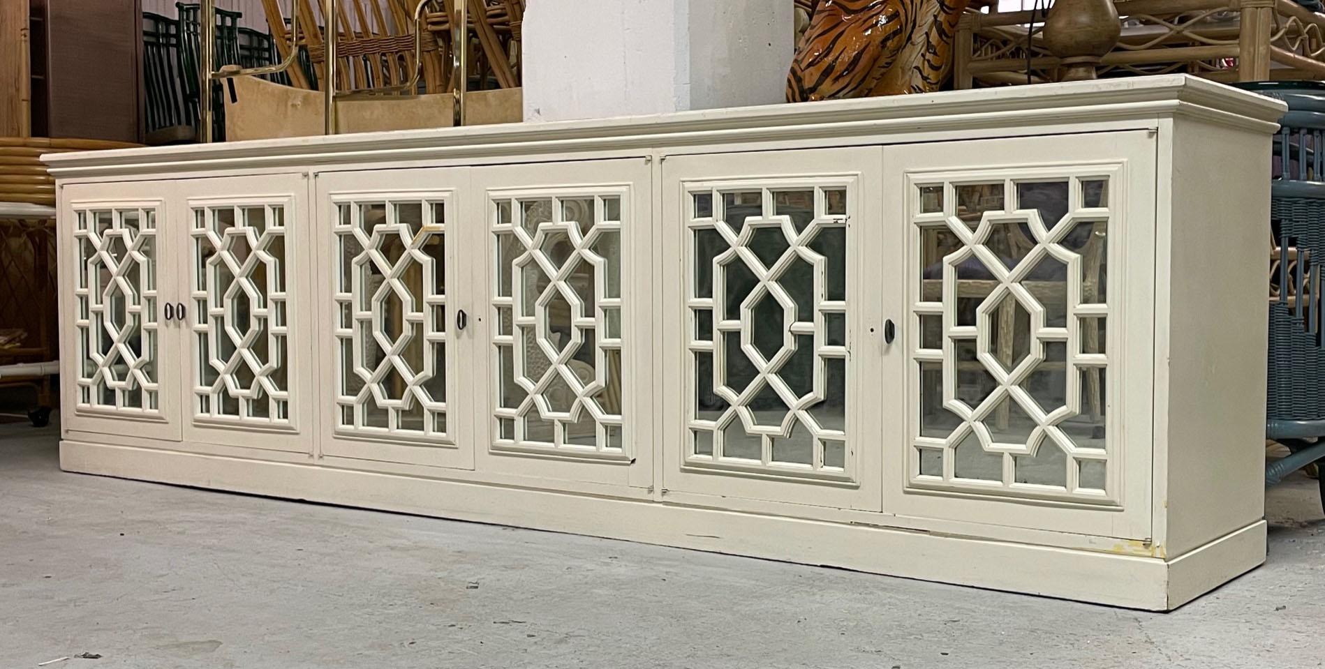 Large solid wood credenza features triple double door storage sections. Mirrored front doors overlaid in Asian style fretwork. Good structural condition with scuffs and marks to the original finish. Structurally sound and drawers doors operate