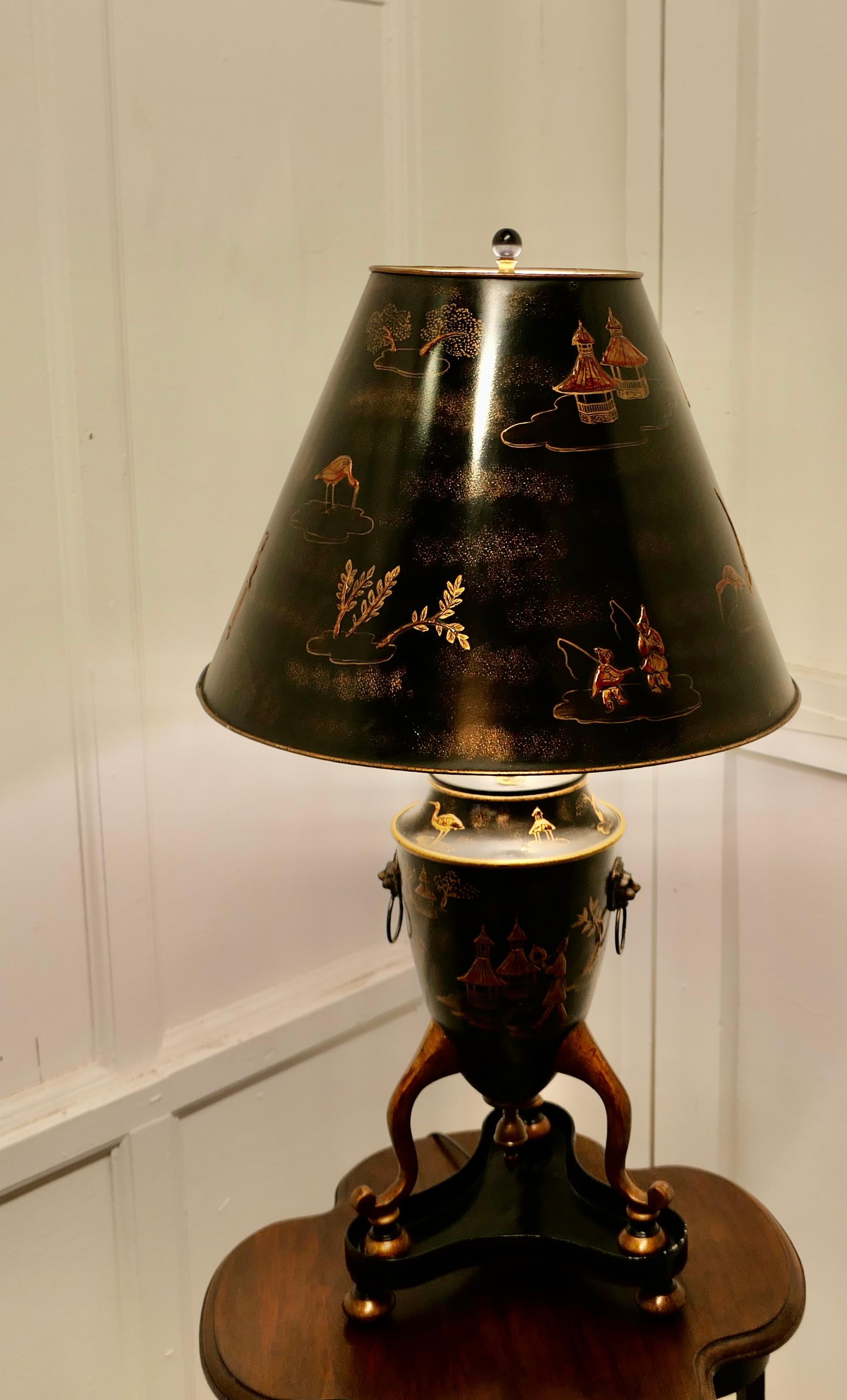 Large Chinoiserie Toleware Table Lamp, Black and Gold Lacquer

A Large Stunning Lamp with it’s original shade is in the style of a Georgian Japanese 3 Footed Urn standing on a Plinth, it has brass mask and ring handles 
Both the lamp and the shade