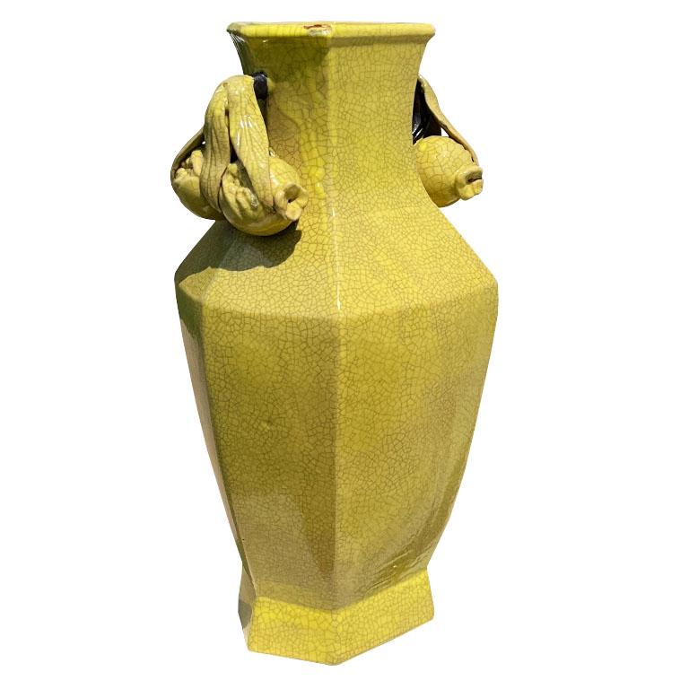 A large 6-sided ceramic yellow chinoiserie vase. Created from heavy clay, this ceramic geometric vase has a wide body and narrow neck. The vessel is glazed in a bright yellow craquelure paint. On each side of the neck at the top, are two applied