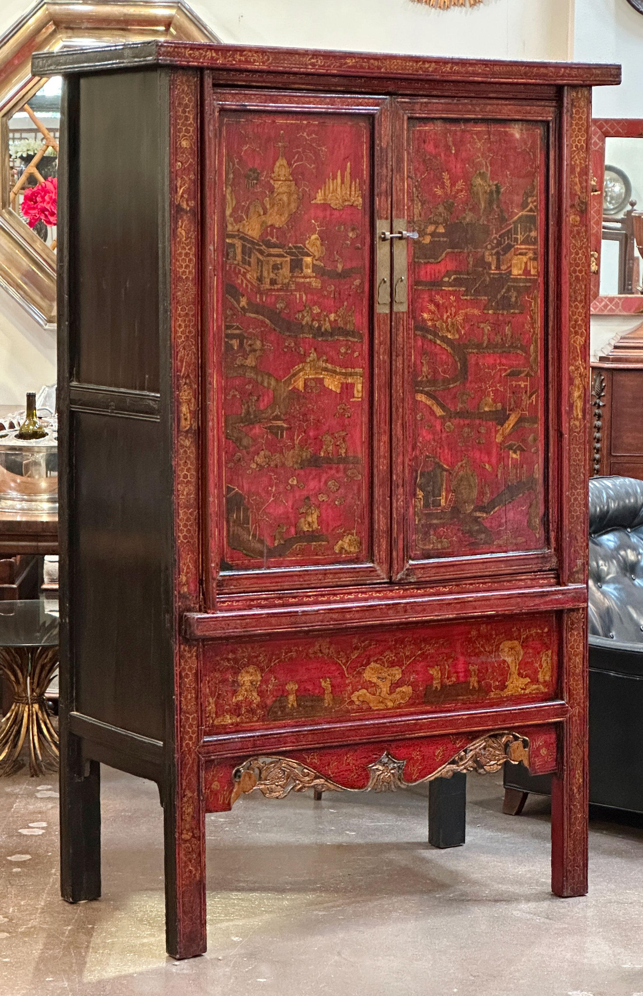 Fino armario o gabinete de principios del siglo XX, de estilo chinoiserie, lacado en rojo, con tapa moldurada sobre un friso de dos puertas paneladas, cada una con escenas decorativas de palacio doradas y herrajes originales de latón, sobre un panel