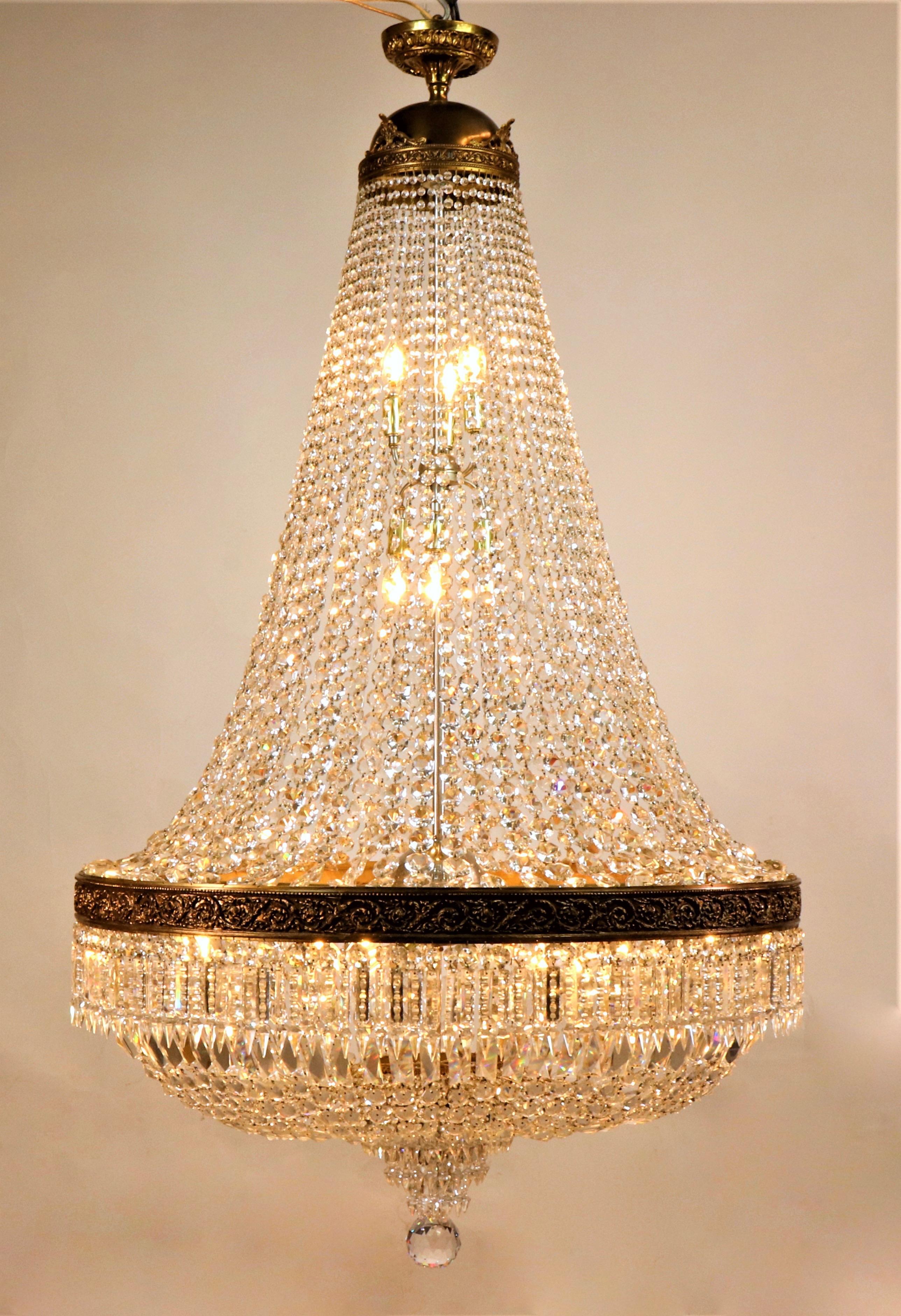 This large-scale circa 1920 Italian Empire style brass, bronze, and crystal chandelier has twenty-two lights for a room requiring substantial illumination. With intricately carved neoclassical details of a brass palmette motif crown with a bronze