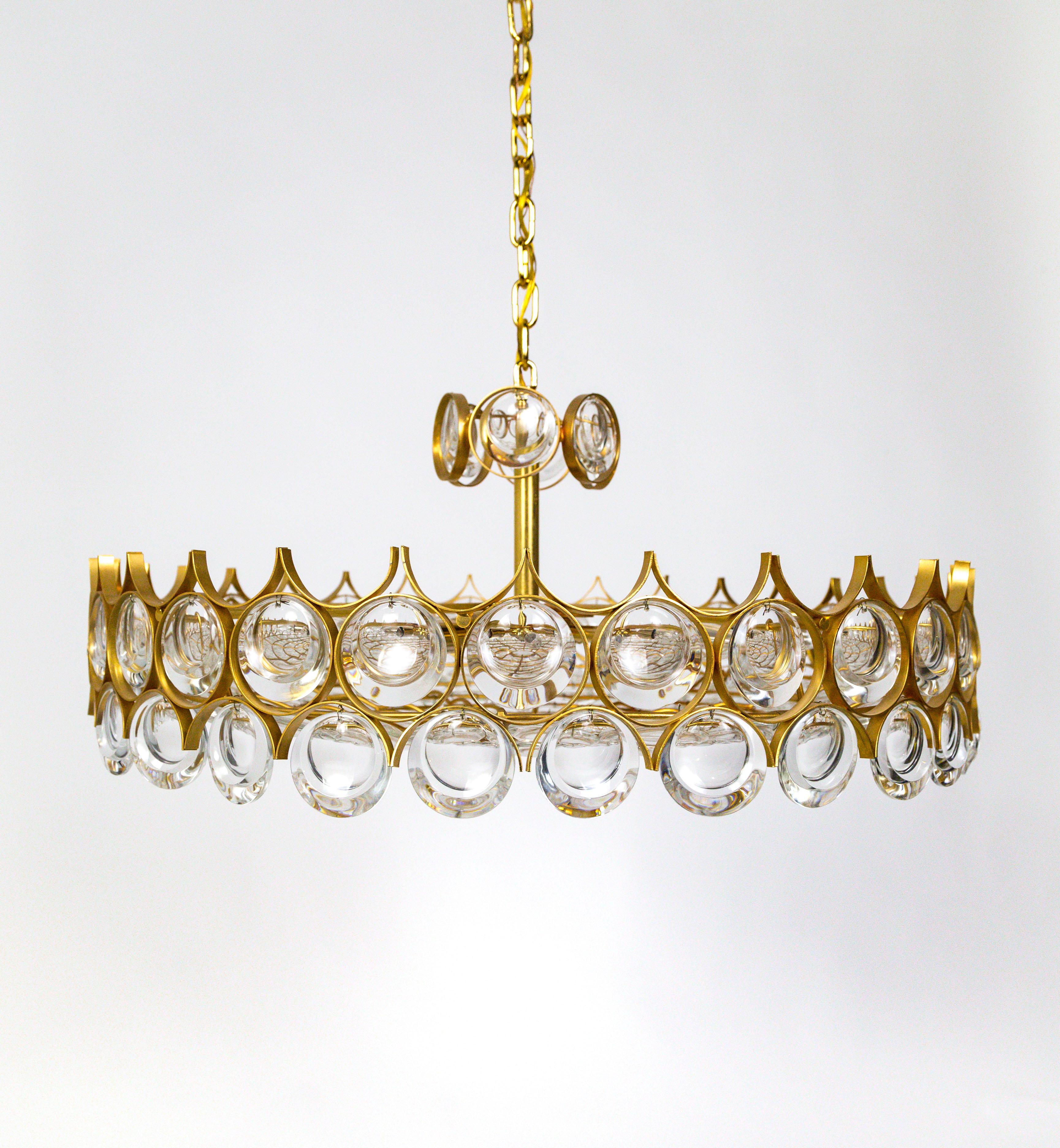 An elegant chandelier filled with dangling and strung, optical lens crystals in a gold armature forming a streamlined, modern shape. Created by Palwa of Germany in the 1960s.
With 9 candelabra lights, newly rewired. 27