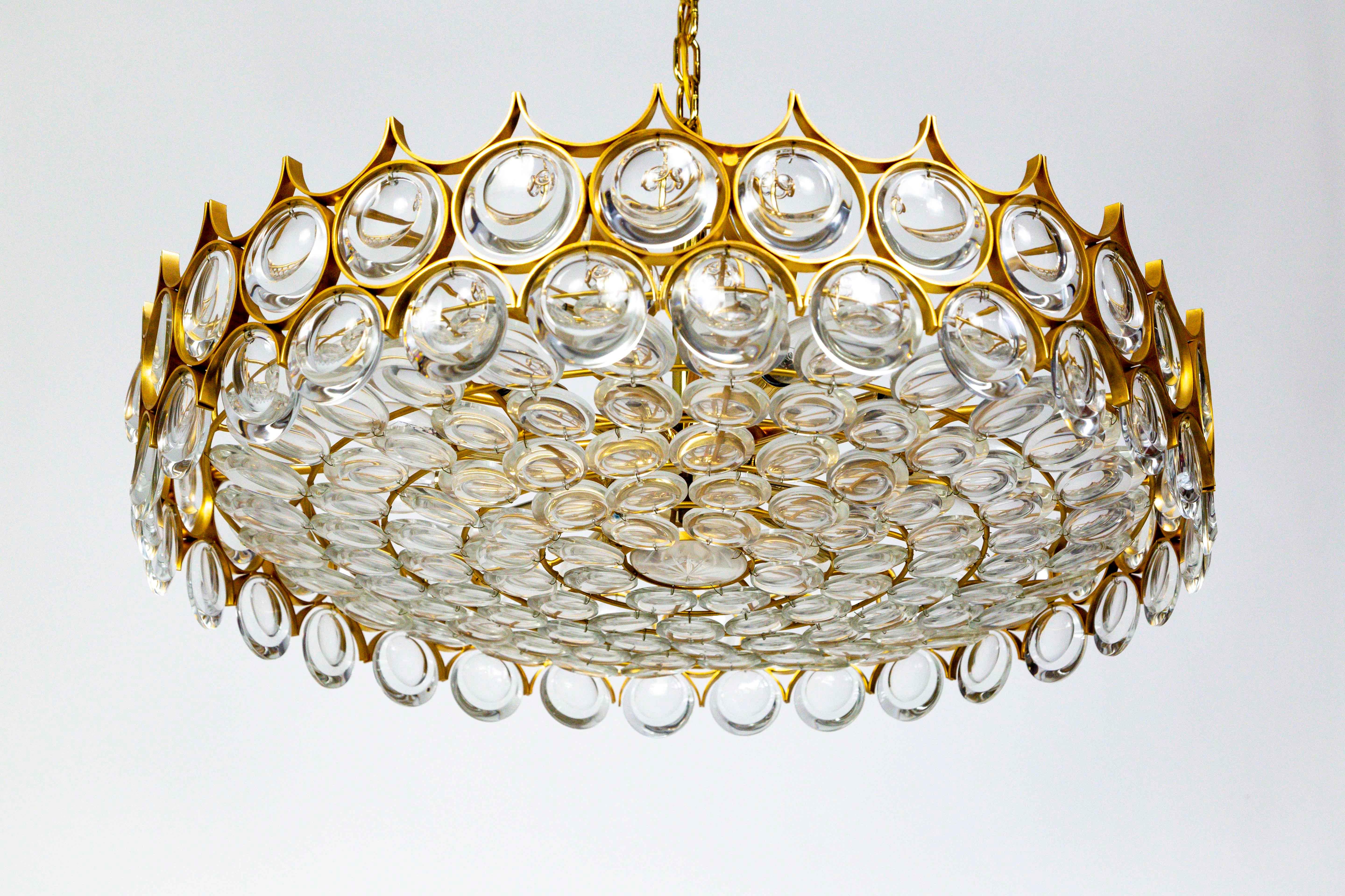 An elegant chandelier filled with dangling and strung, optical lens crystals in a gold armature forming a streamlined, modern shape. Created by Palwa of Germany in the 1960s.

9 candelabra lights, newly rewired. 27