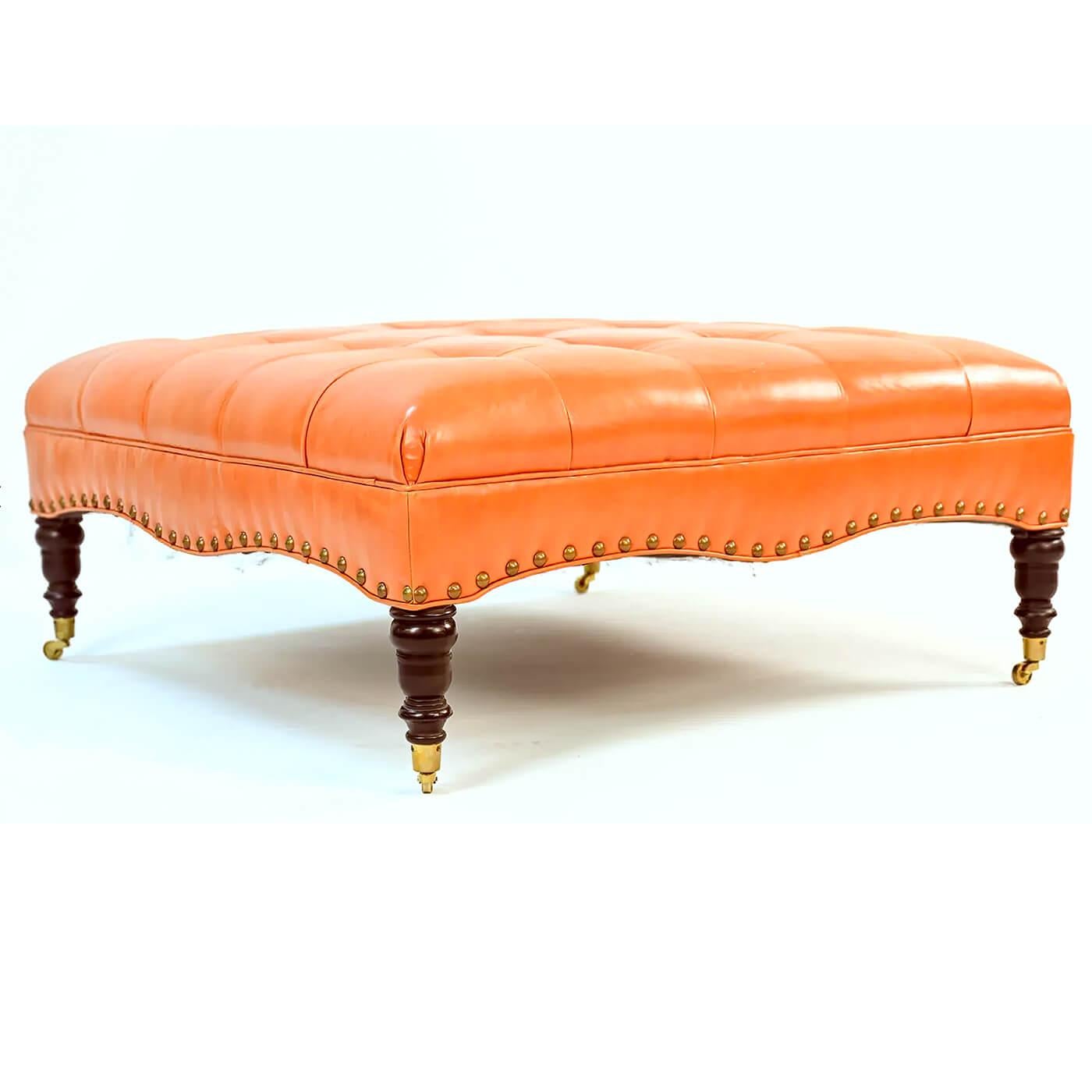 A large classic tufted orange leather upholstered square ottoman with serpentine rails having large brass nailhead details and raised on turned legs with brass caster feet.

Late 20th century 

Dimensions: 42.5