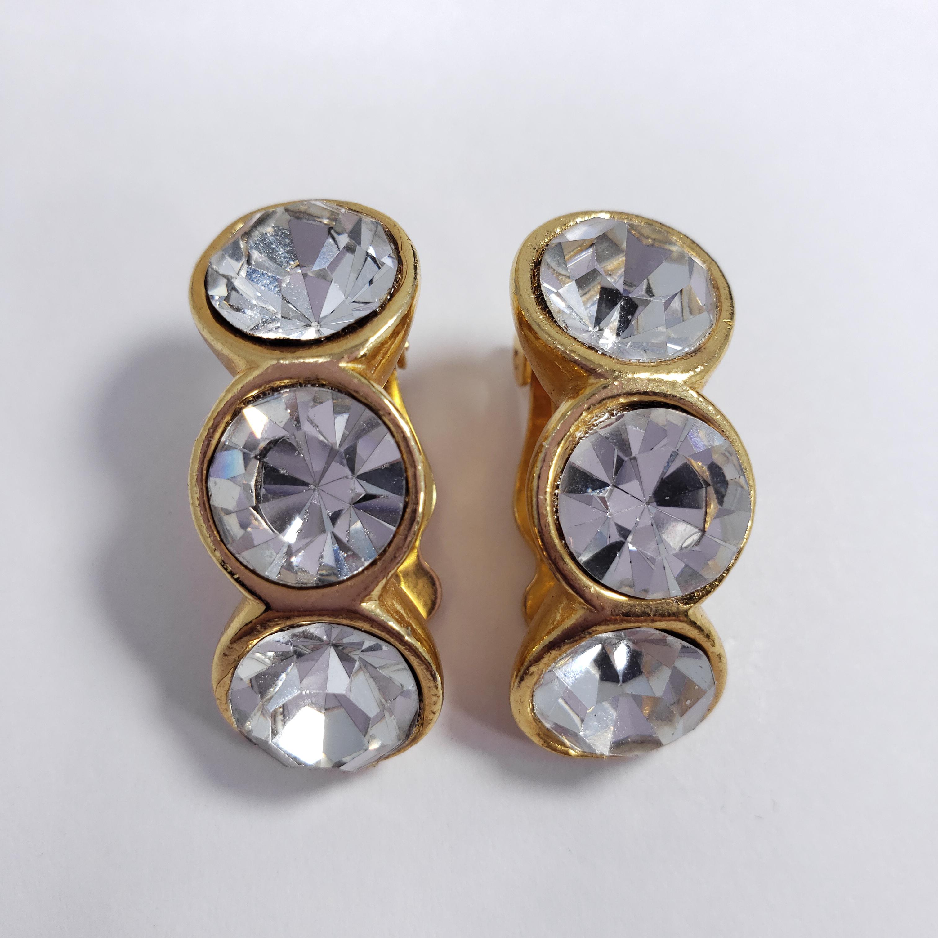 A pair of stylish clip on earrings. Each earring features three large faceted clear crystals, set in a curved row. Set in gold-tone metal. 