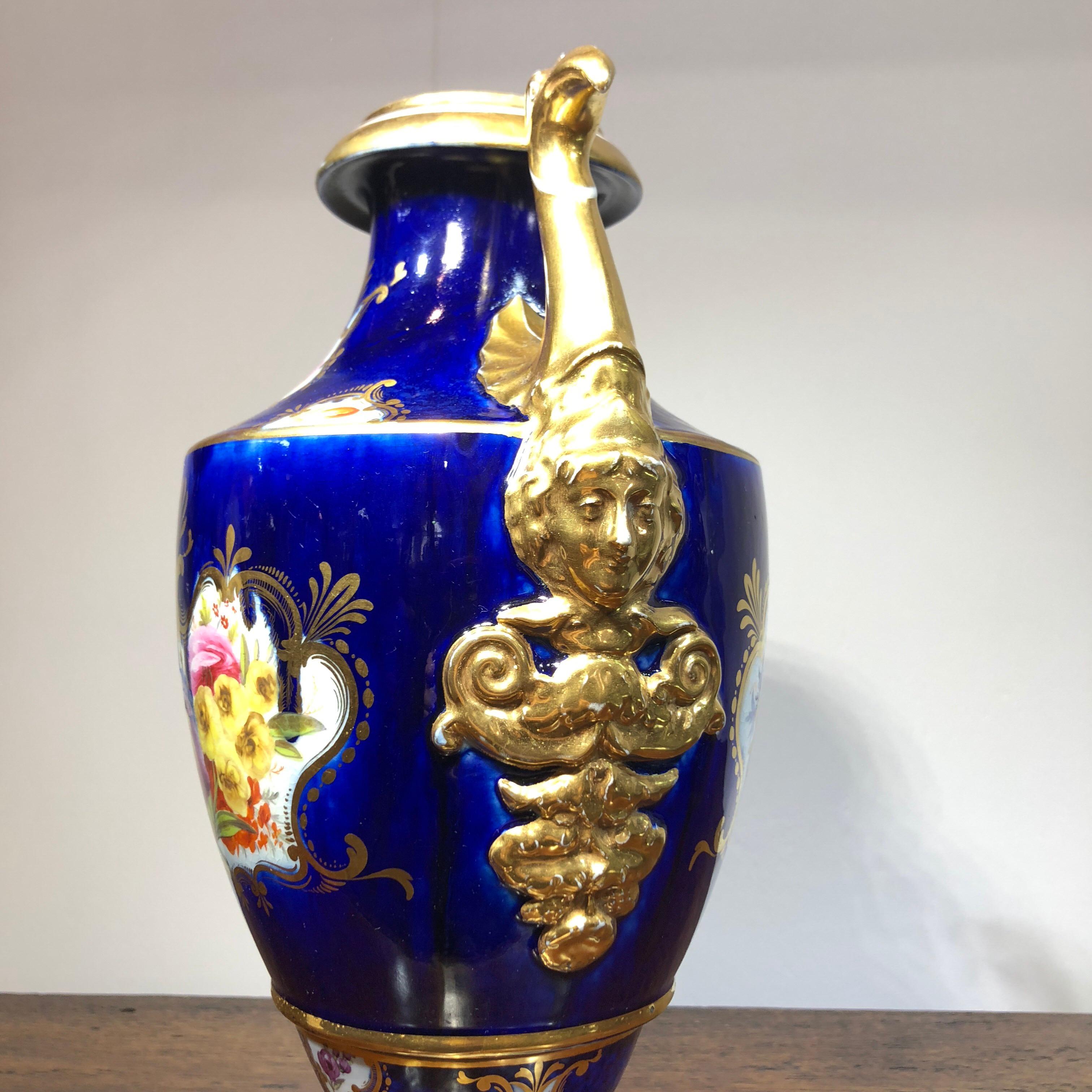 Large Coalport vase, the classic form made extraordinary by large birds head handles rising to the lip with classical mask beneath, well decorated with panels of colorful flowers on a blurred scale-blue ground.
Unmarked, circa 1805.