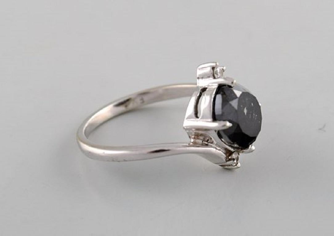 Large cocktail ring in 14 carat white gold with oval facet cut black diamond of approx. 3.50 ct. flanked by two brilliant-cut diamonds. Mid 20th century.
Diameter: 17.5 mm.
US size: 7.
In very good condition.
Stamped.
Color: Top Cape (K).
Clarity: