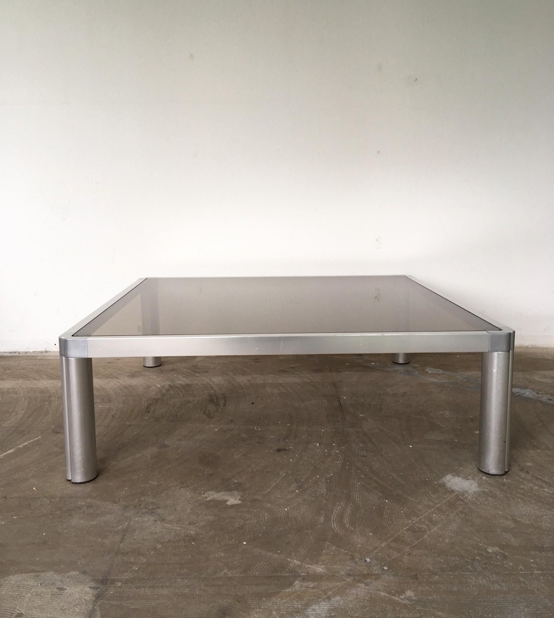 This large coffee table, model 100, was designed by Kho Liang Ie for Artifort in 1974. It features a smoked glass table top and an aluminium base. Very nice industrial piece which remains in great condition.