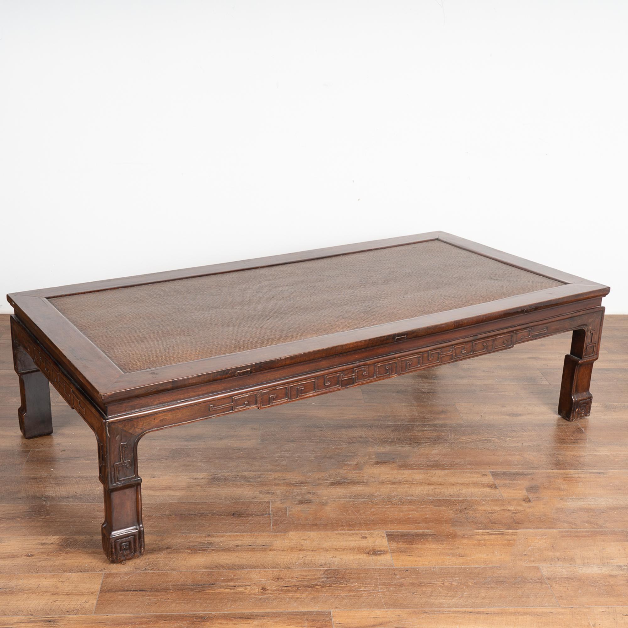 Large Chinese coffee table with carved skirt and legs with rattan top and traditional lacquered finish.
This handsome coffee table is strong, stable and ready for use. Wear related scuffs, scratches, minor separation (at corners) are a reflection of