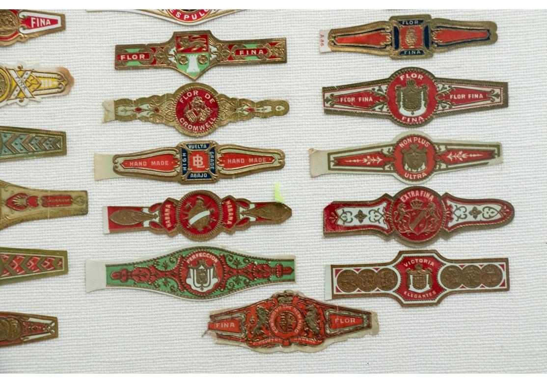 A large collection of various multi-colored and gilt cigar bands mounted on white linen. Including some Habana (along the top and others).
in gilt frames 20 x 18 1/2