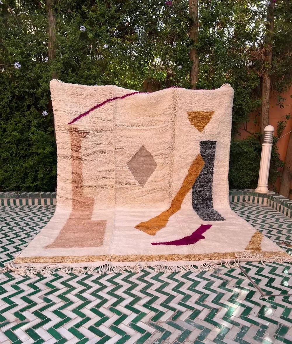 This large, modern handwoven Moroccan rug was made by hand by skilled artisans in the Atlas Mountains. It features a high quality, neutral cream wool base with a graphic, multi-colored abstract design unique to Moroccan style. Handmade on a loom