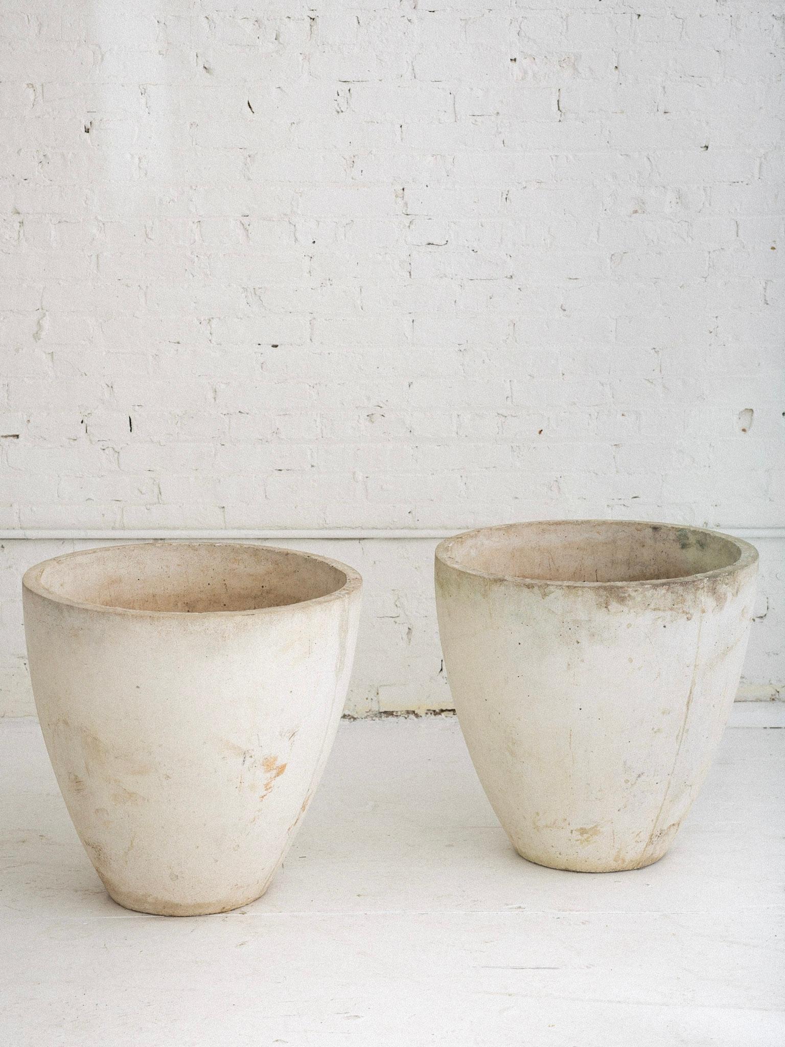 A pair of large concrete cast stone planters. Tapered cylinder silhouettes. Features drainage holes. Chalky white / grey finish with a weathered patina. Heavy solid pieces.