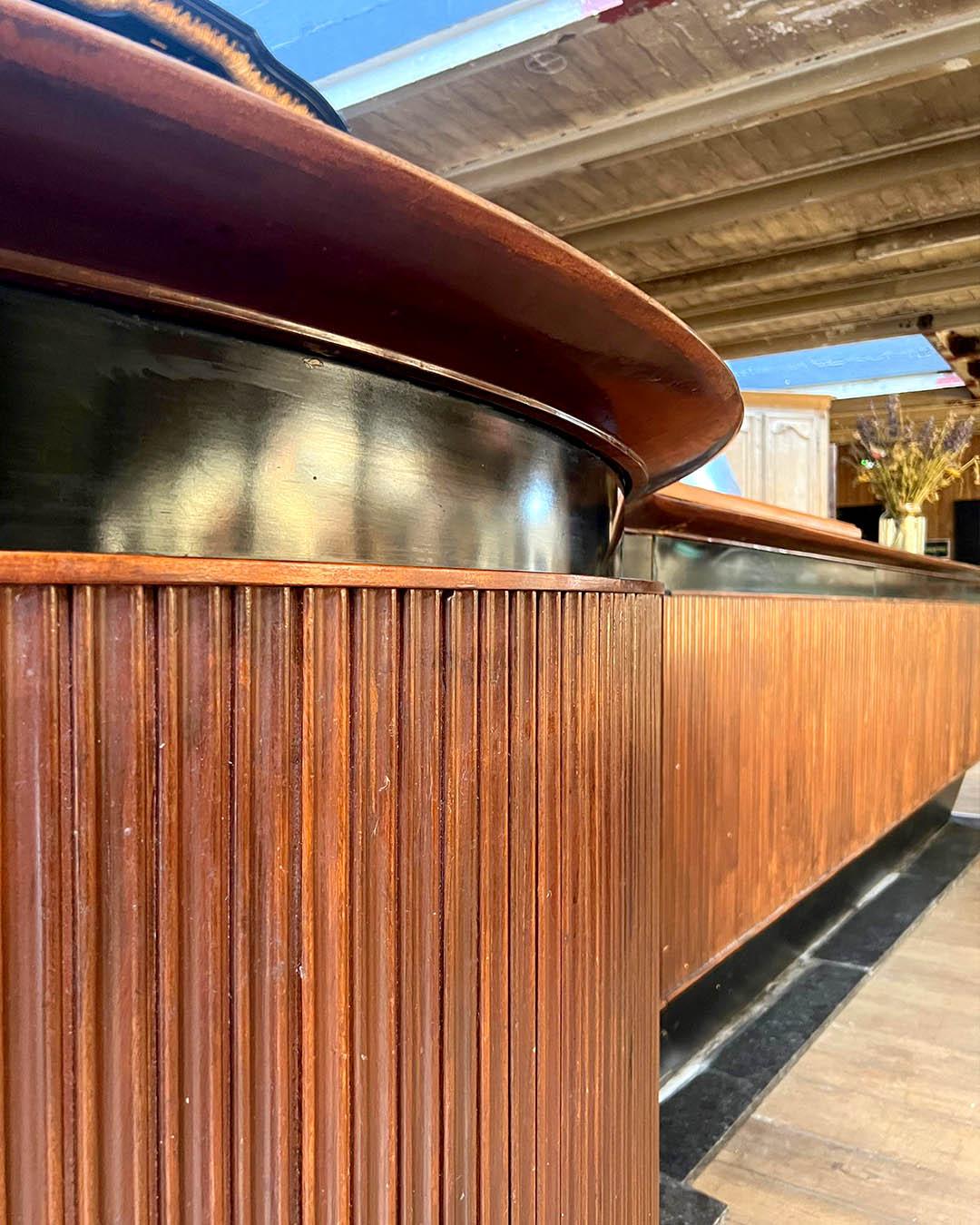Impresionante bar contemporáneo a gran escala con una fachada de madera bellamente estriada y un llamativo mostrador de efecto palisandro. El diseño combina elegancia y funcionalidad, con un frontal suavemente curvado y una amplia zona de servicio