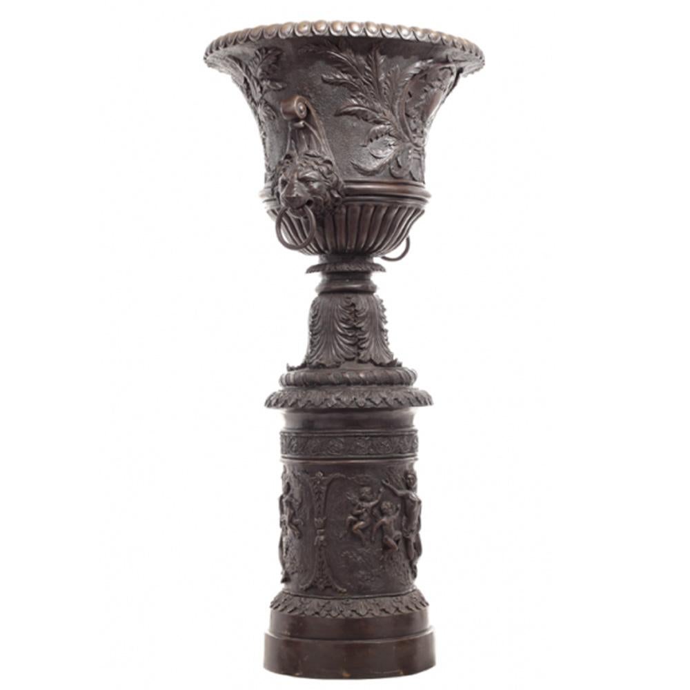 A large contemporary classical themed cast bronze urn on pedestal with lion handles. Featuring a tall silhouette, this exquisite urn was cast with the traditional lost-wax technique (à la cire perdue), allowing a great precision in the details.