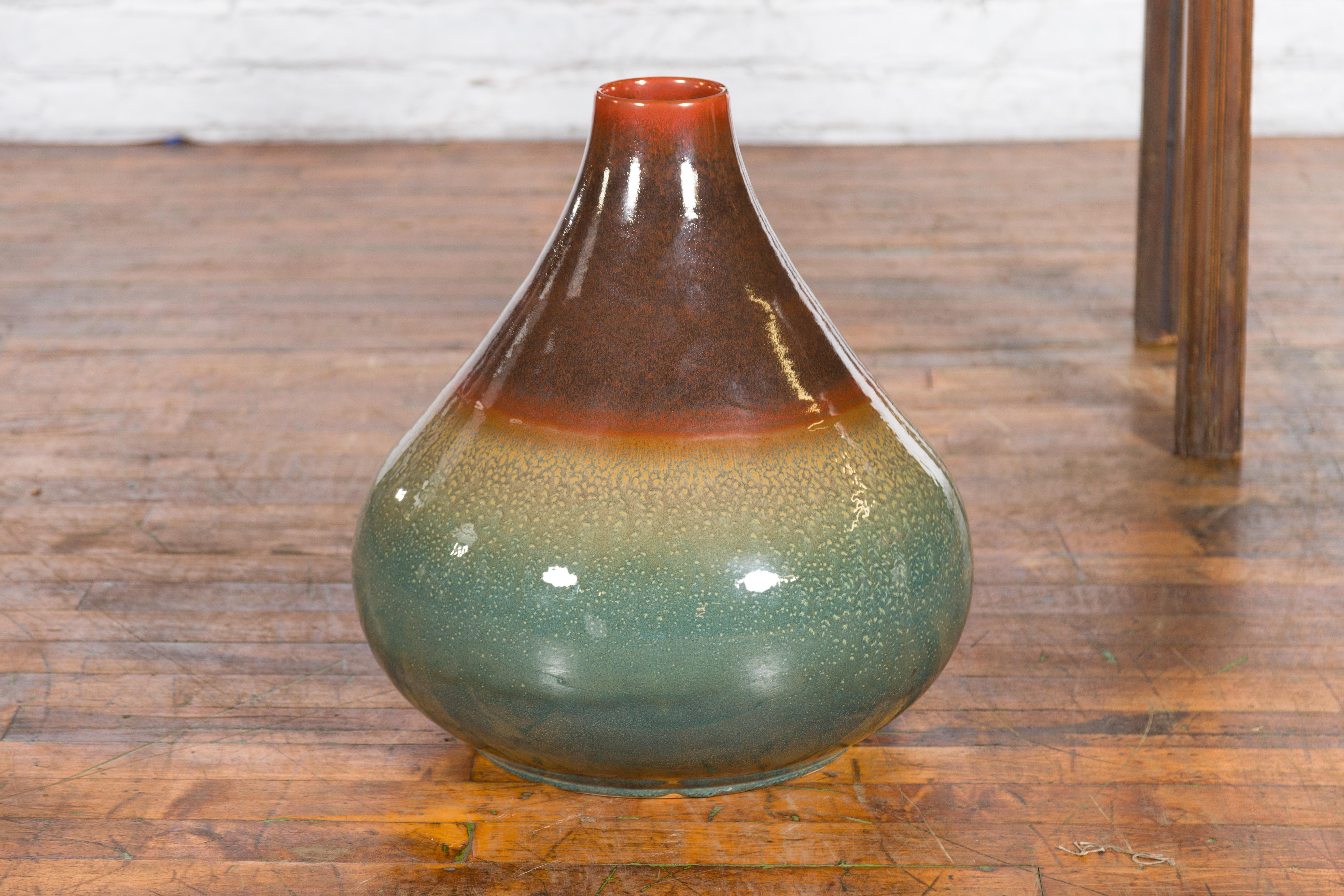 A large contemporary Northern Thai jar from the Prem Collection, with green and brown glaze. Charming our eyes with its pure lines and complimenting colors, this vase was born in Chiang Mai, northern Thailand. Featuring a narrow neck with a 3.5