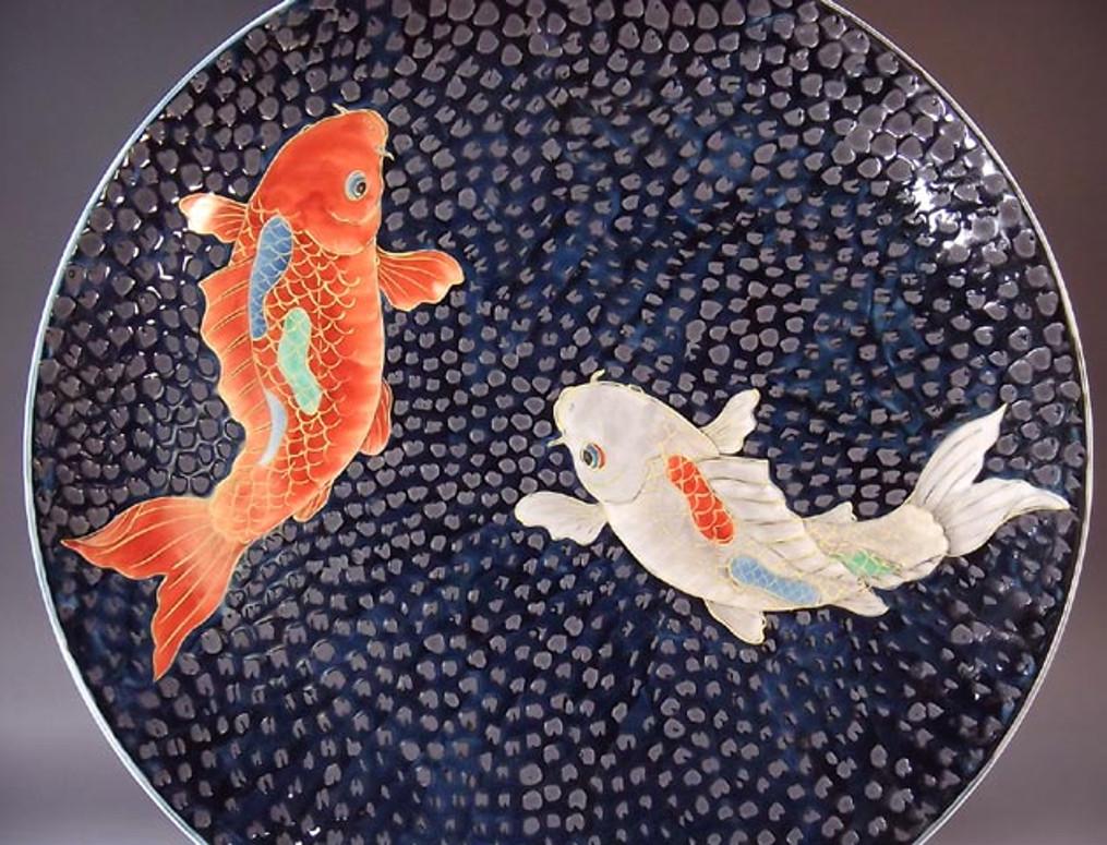 Exquisite Japanese contemporary large gilded, hand painted and dimpled porcelain charger by acclaimed master porcelain artist, depicting two elegant carps in red and cream, with intricate gold details, swimming against a dimpled black background.