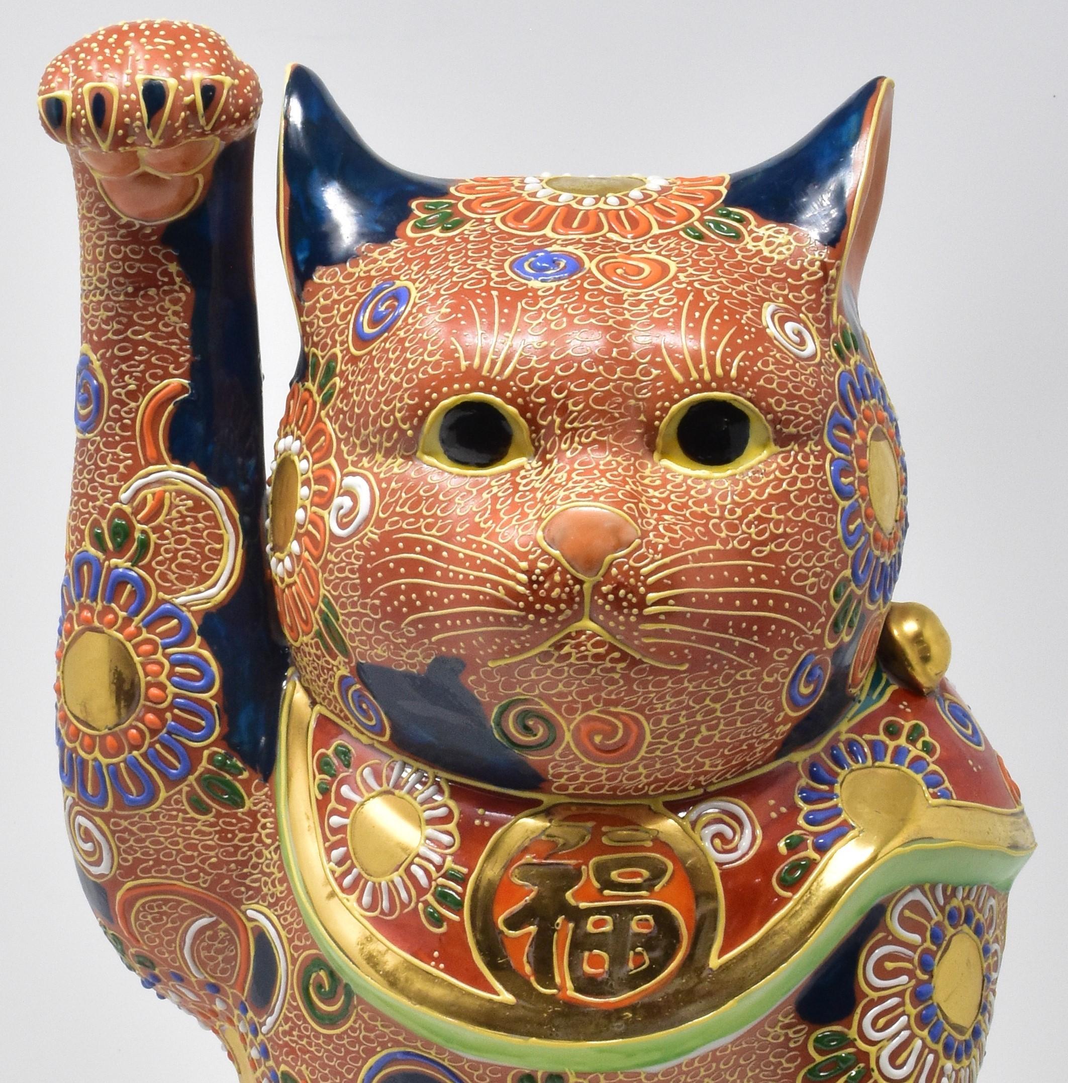 Large contemporary Japanese lucky cat (maneki neko,) a gilded and extremely intricately hand painted porcelain lucky cat raising his right paw, from the Kutani region of Japan. This cat in orange/brown, red, green and dark blue is adorned with