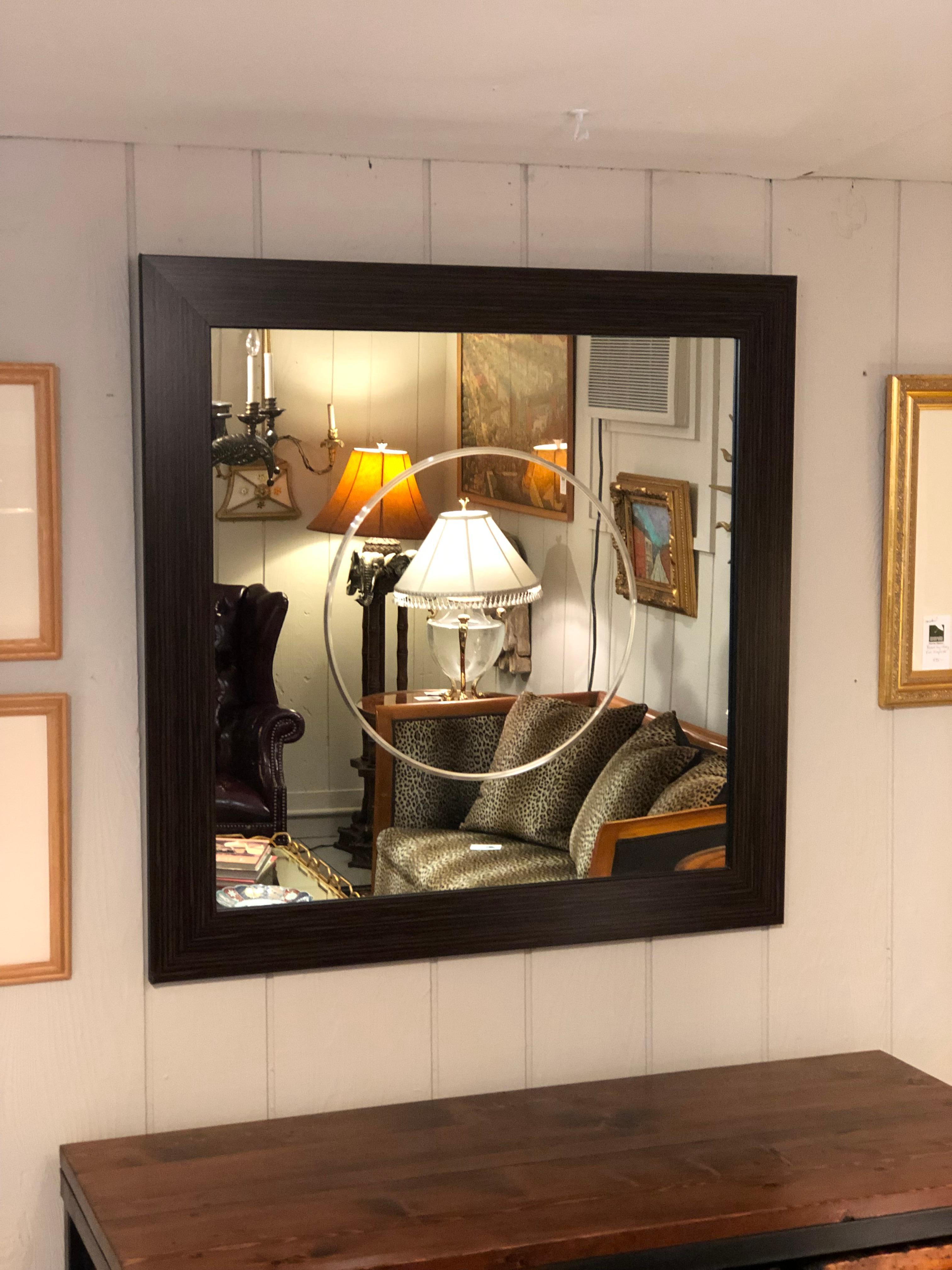 A stunning contemporary wall mirror having simplicity and clean lines with the center of the mirror decorated with a large etched circle. The frame of the mirror is a striated wood faux leather.