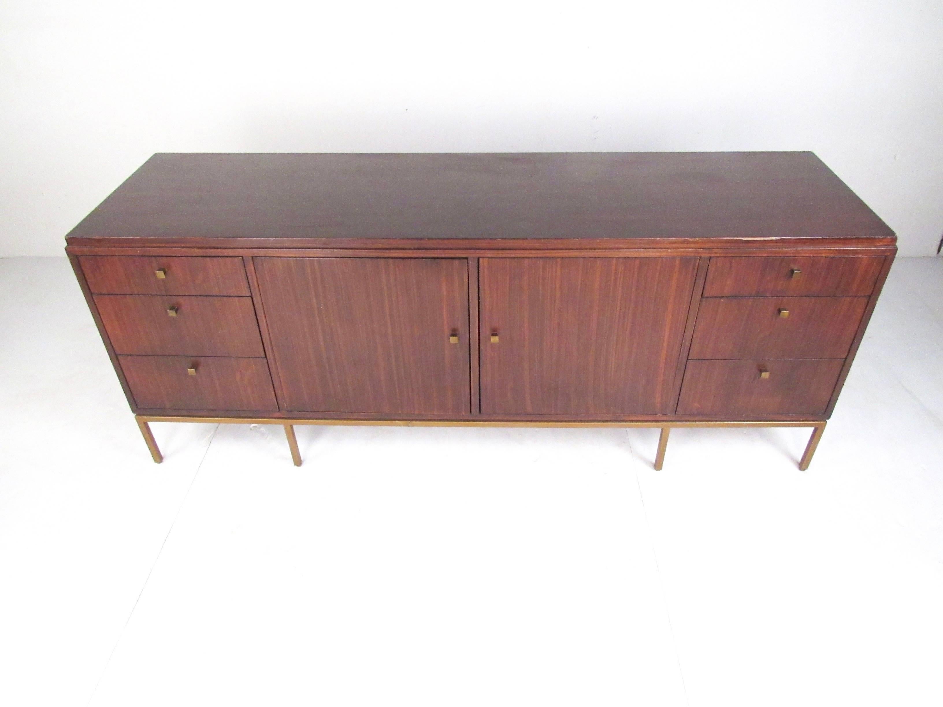Beautiful Mid-Century Modern style sideboard features plenty of room for storage within its six large drawers and four shelves hidden behind two cabinet doors. Sleek design with unique brass pulls and a solid brass base with eight legs. Sturdy