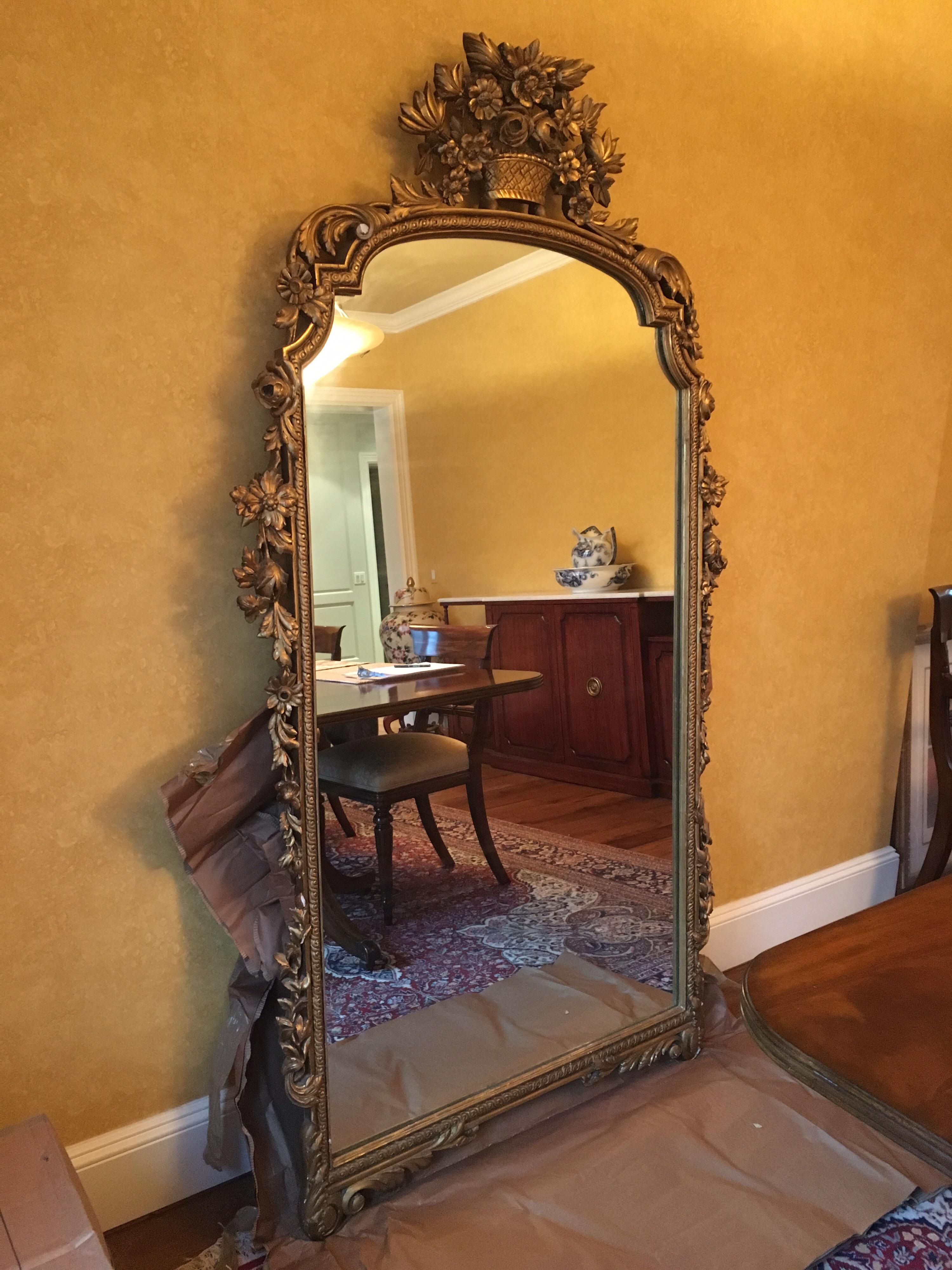 Large Continental gilt parlor mirror, 20th century, flower basket crest and pierce carved detail, gilded gesso. Two available, sold separately. Loss to gilt and small chips to frame have broken off in some areas. Notice top left corner in image