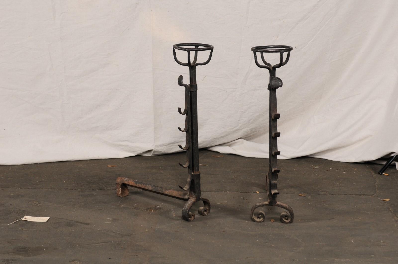 Large continental hand forged iron andirons with port warmers and adjustment notches, circa 1900.