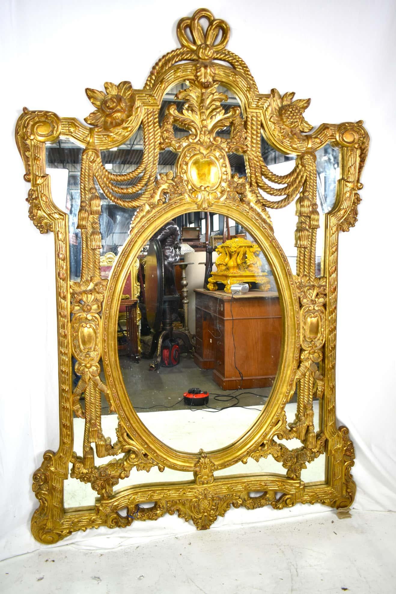Un gran e impresionante espejo antiguo con un marco ornamentado dorado y muy decorado, con una excepcional cresta de volutas y follajes tallados, que remata un espejo flanqueado por bordes de volutas y cuerdas.