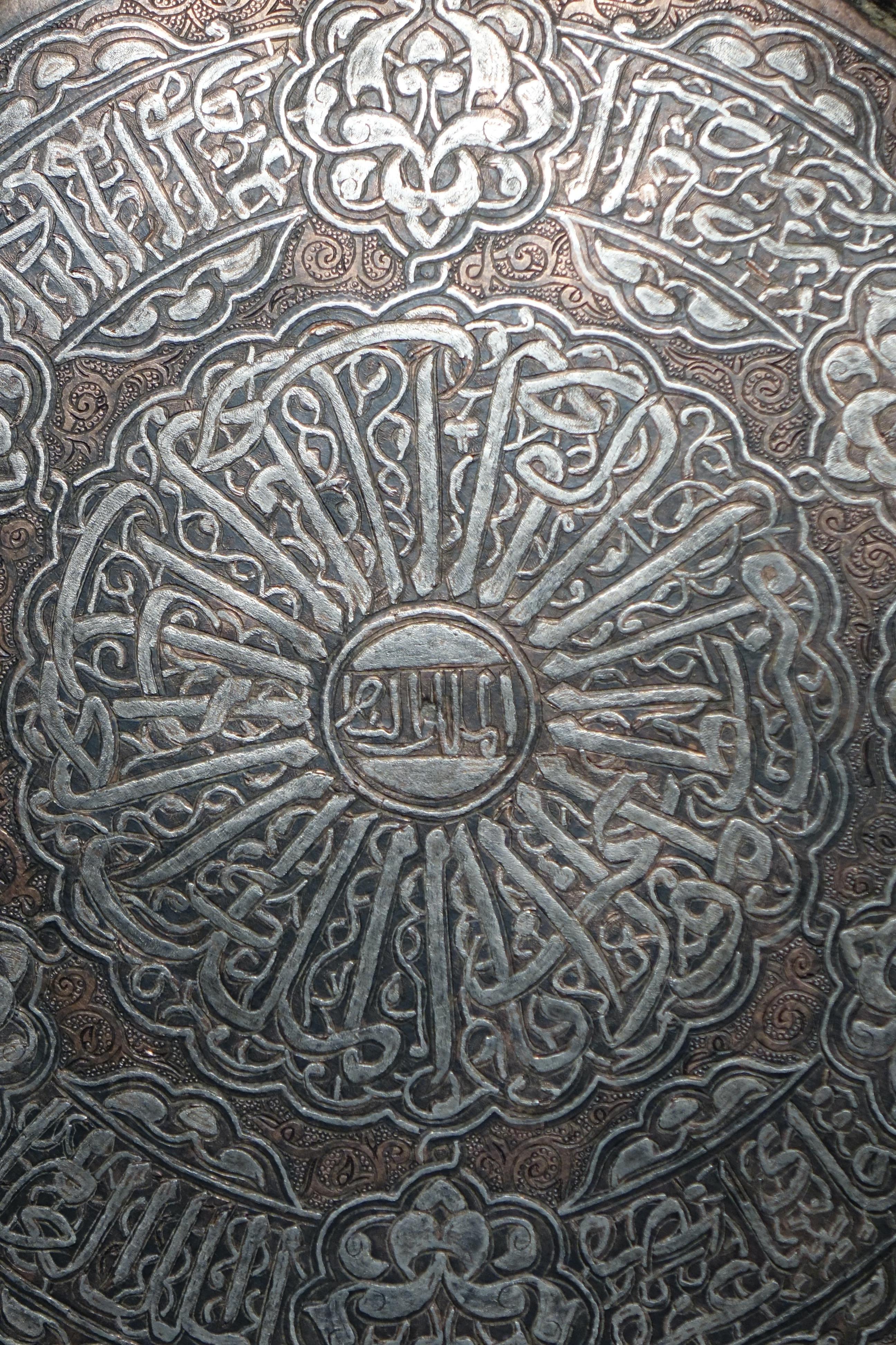 Grande bacino in rame damascato d'argento decorato con volute, arabeschi e fogliame, che circonda le cornici di scrittura del thuluth.
Sul retro è stato saldato un attacco che permette di appenderlo.
Egitto, XIX secolo. o prima.

