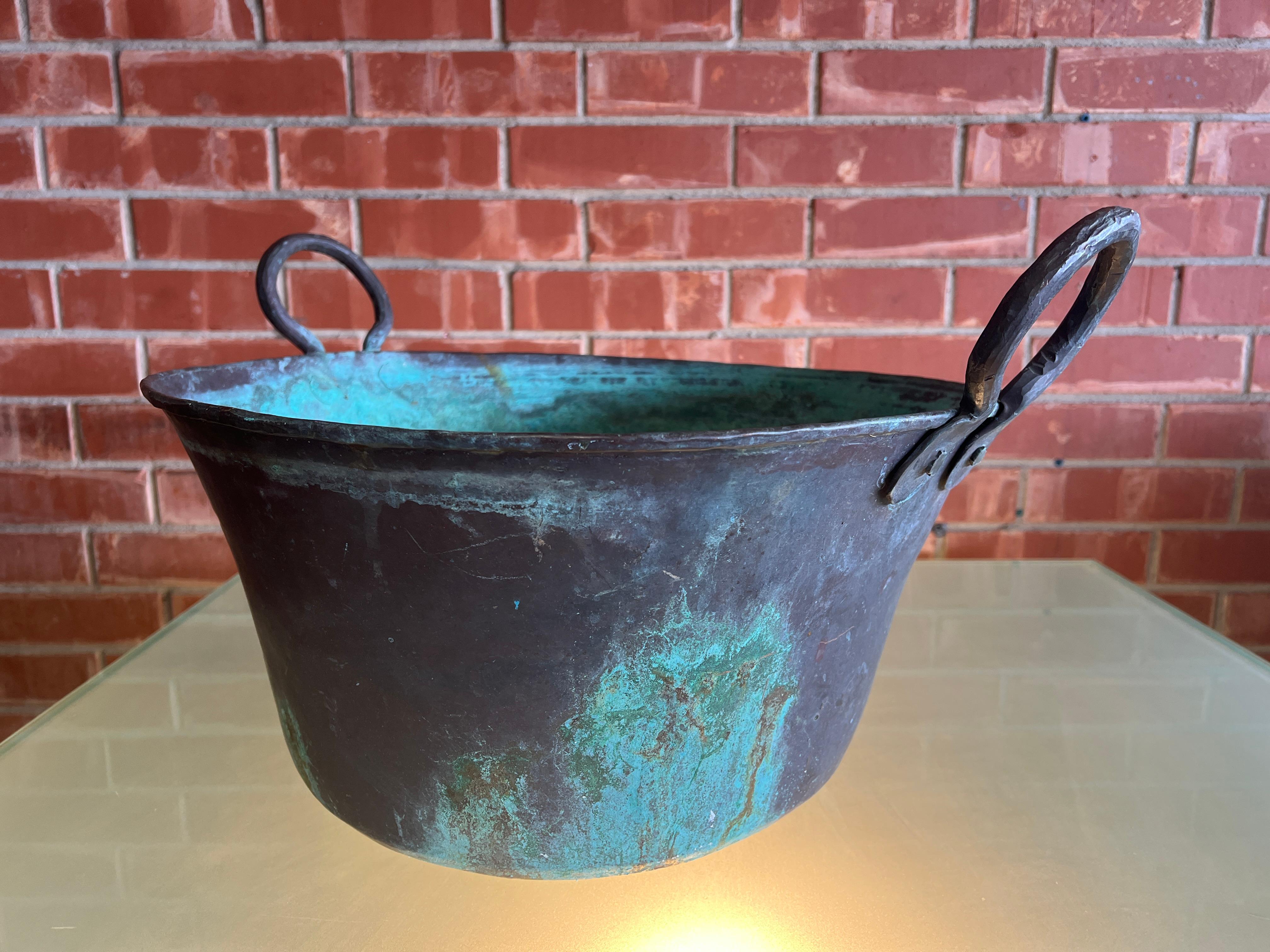 This large hammer copper pot or garden planter boasts circular handles on either side, providing a sturdy grip for effortless lifting. Its surface is adorned with a delightful green patina, both inside and out, adding a touch of rustic charm and