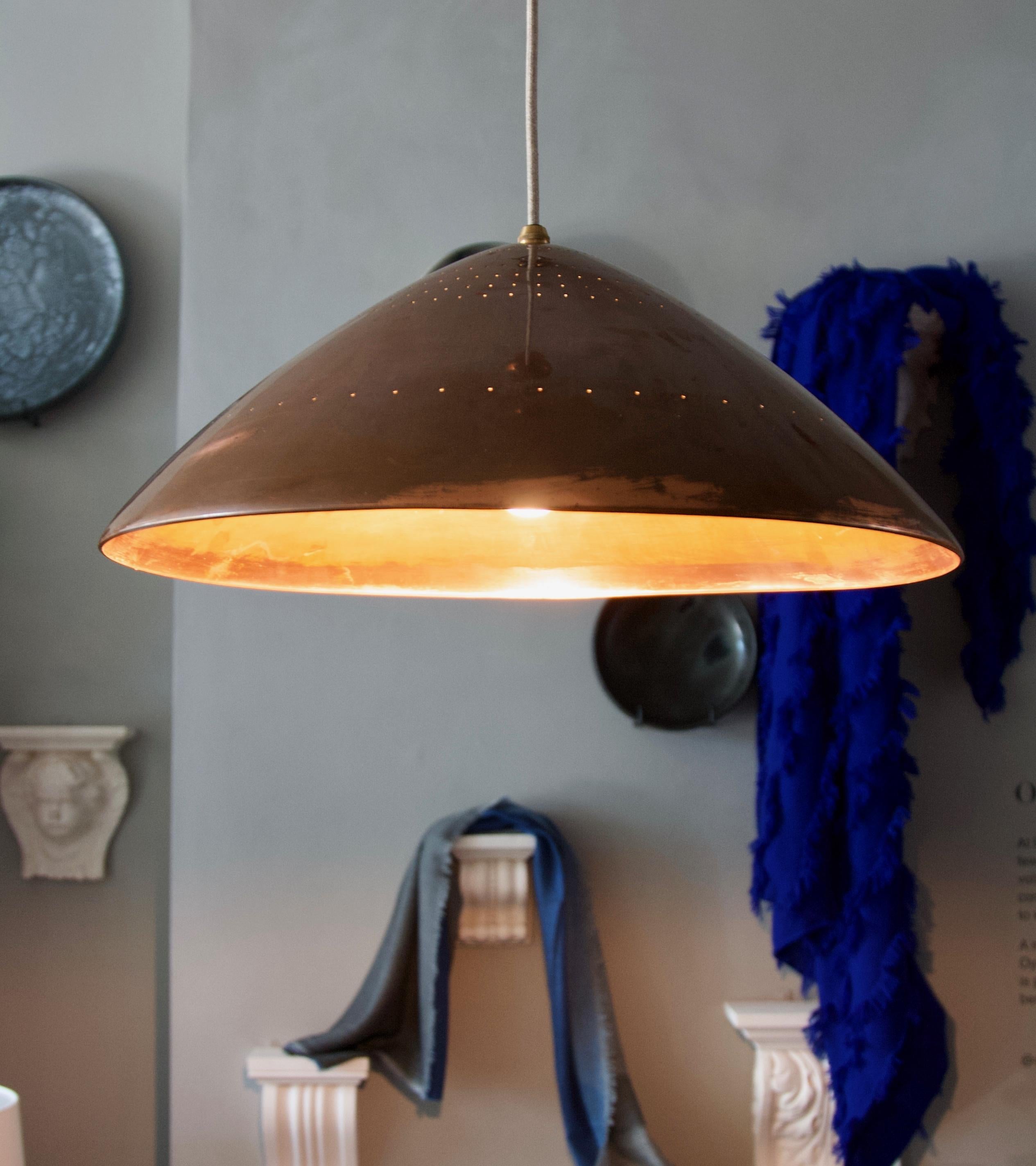 A large solid copper ‘rise & fall’ pendant light, most probably designed and made in Germany, circa 1960.
The elegant and unusually shaped shade has been perforated to create a subtle light effect once illuminated. The perforations are along six