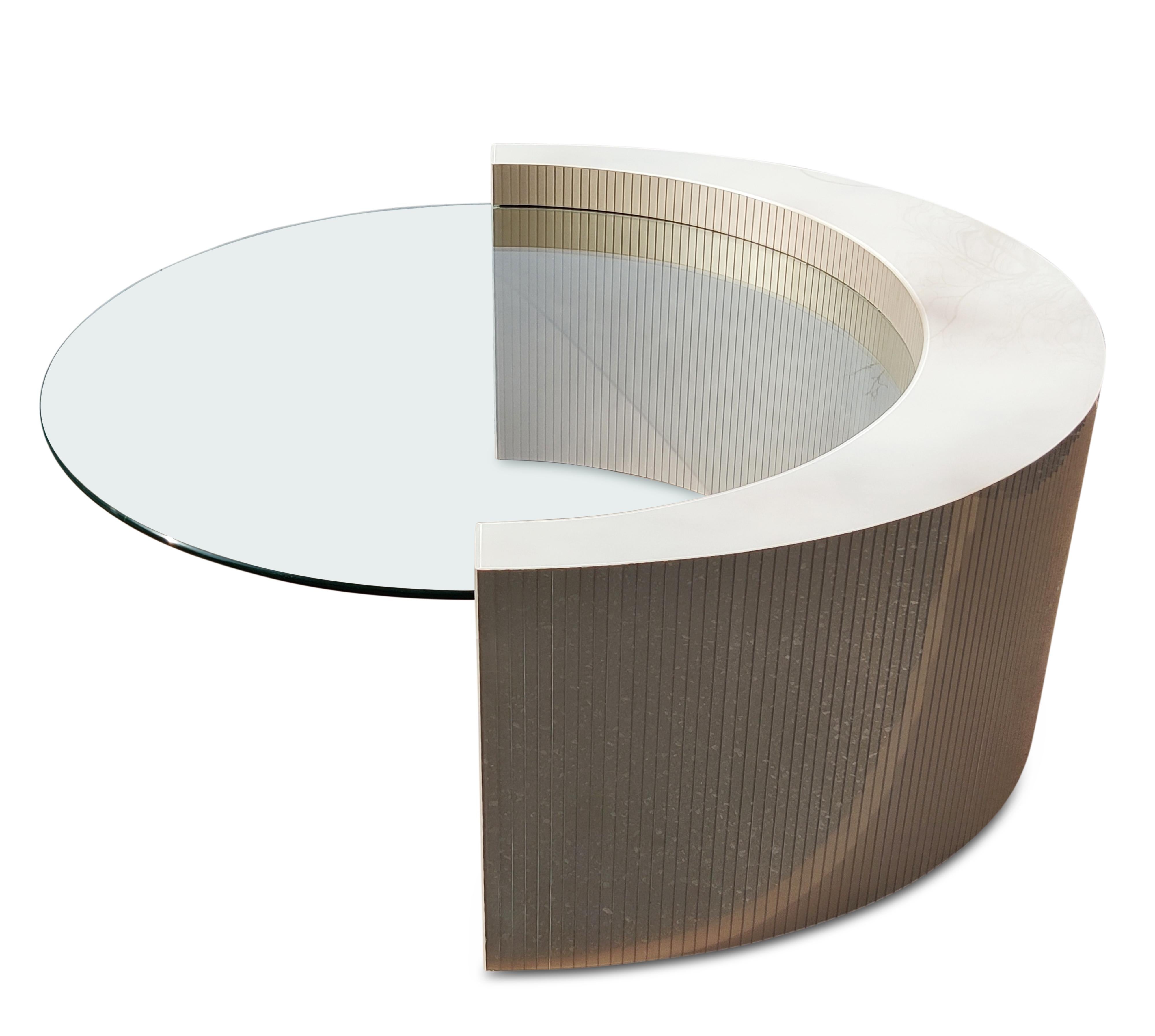 This beautiful coffee table has unique construction. Shaped like a crescent, it has a curved wood frame overlaid with elegant gray acrylic strips. About 3 inches below the top of the crescent, there is a slot in the base which houses a removable