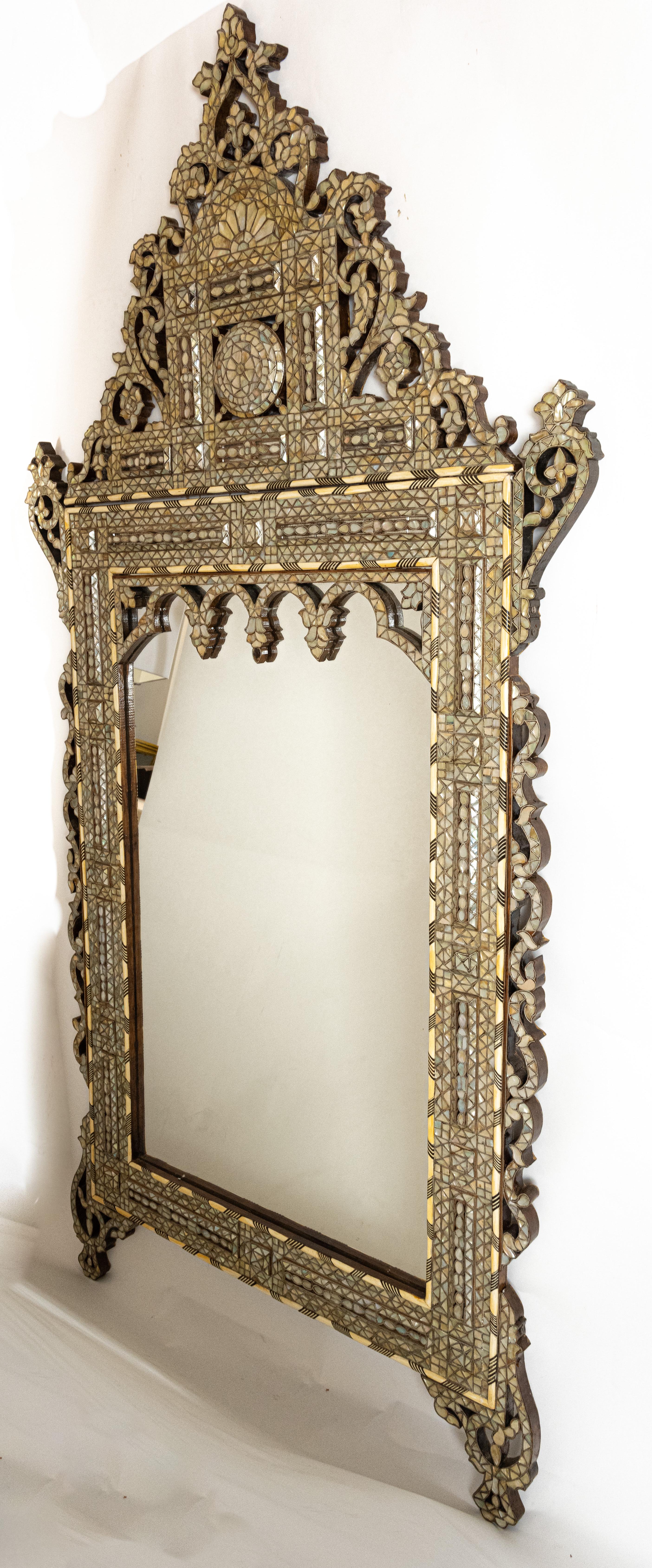 A large crested Syrian mother of pearl mirror with bracket feet. Having a rectangular vertical looking glass framed with finely detailed inlaid cedar-like wood. The glass surrounded by inner molding with contrasting composition details. The upper