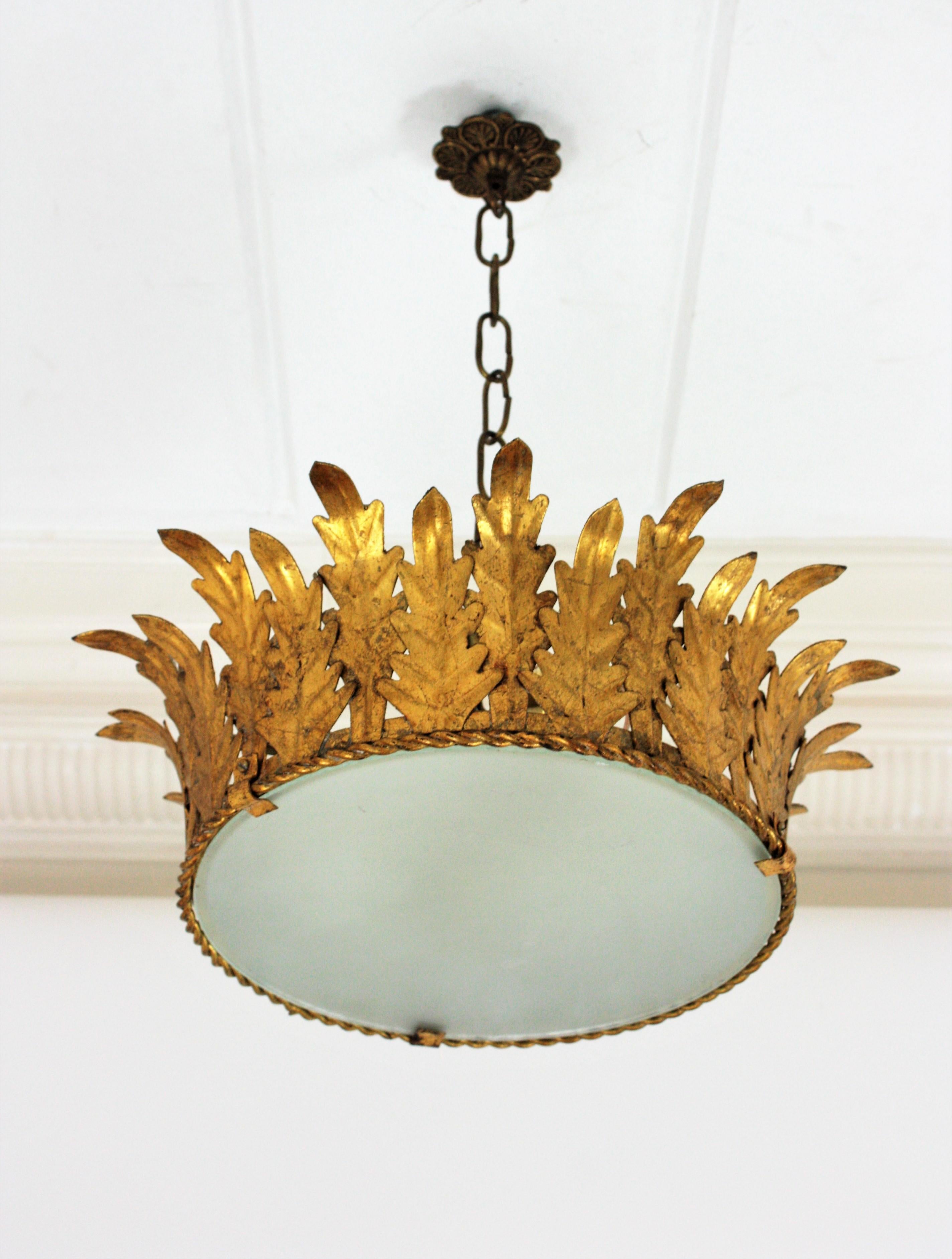 Large neoclassical style hand-hammered gold leaf gilt iron crown flushmount or pendant, France, 1940s.
This elegant ceiling light features a gilt metal structure adorned with foliage motifs. It has a frosted glass diffuser that allows to disperse a