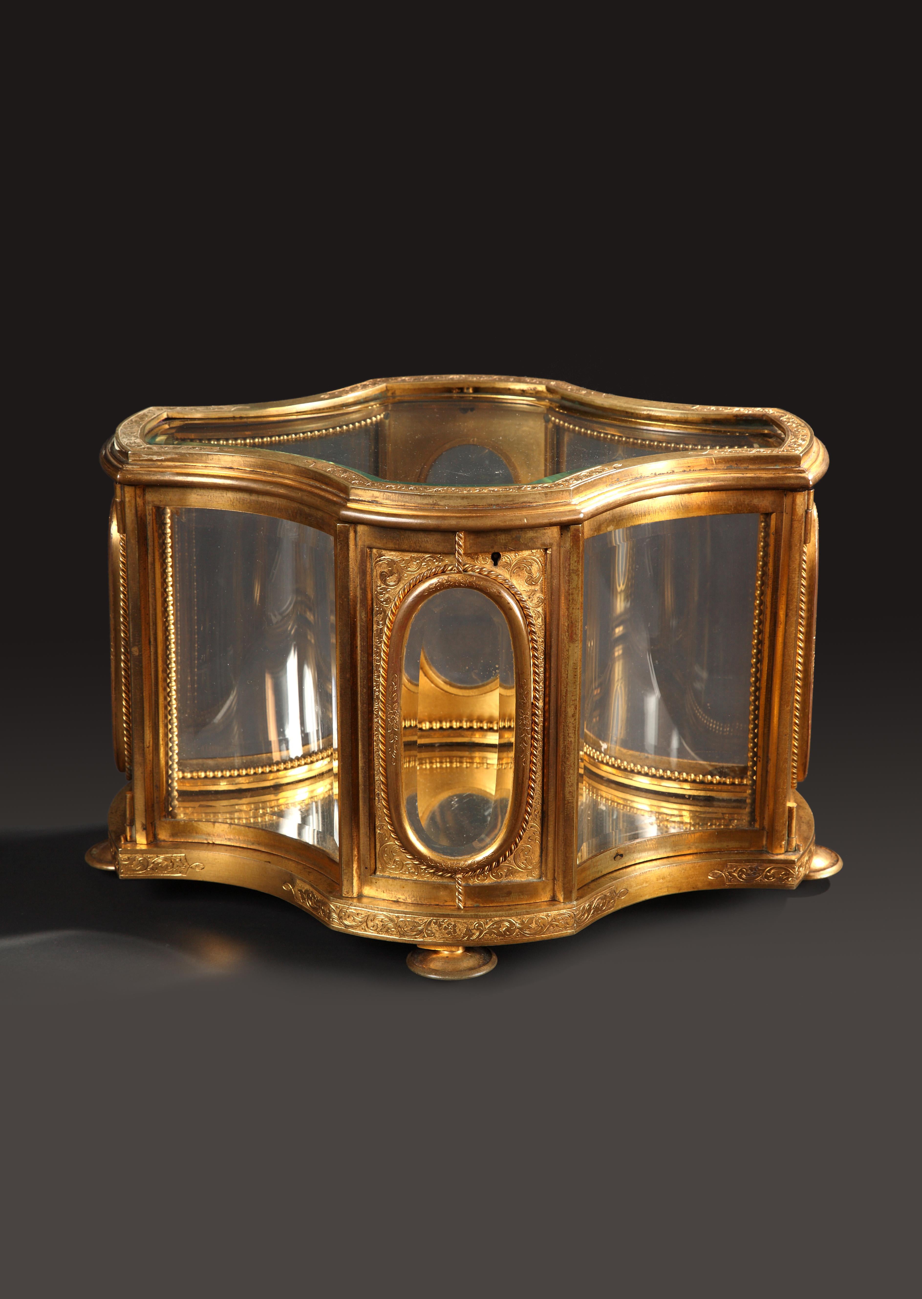 Important display case, with a mirror at the bottom, made in gilded bronze with engraved decoration, with bent and beveled crystal panels. Resting on four toupie feet. The top and the sides can be completely and widely opened.

L’Escalier de