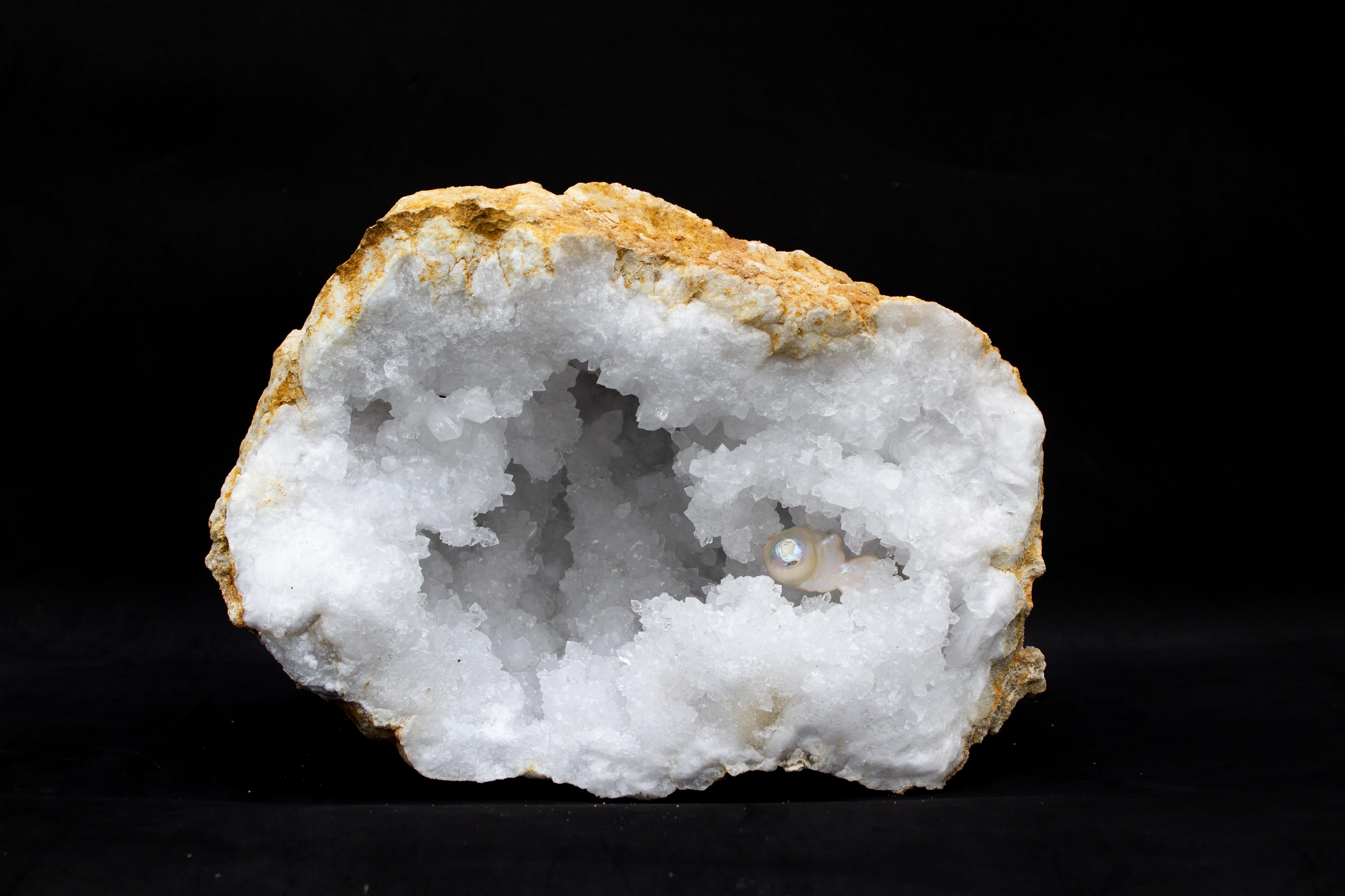 Large white crystal quartz geode with a baroque pearl.

Geodes are formed as gas bubbles within volcanic lava. Crystals slowly grow from minerals with filter into the geode. Over time, the lava flow weathers away to leave the quartz geode buried