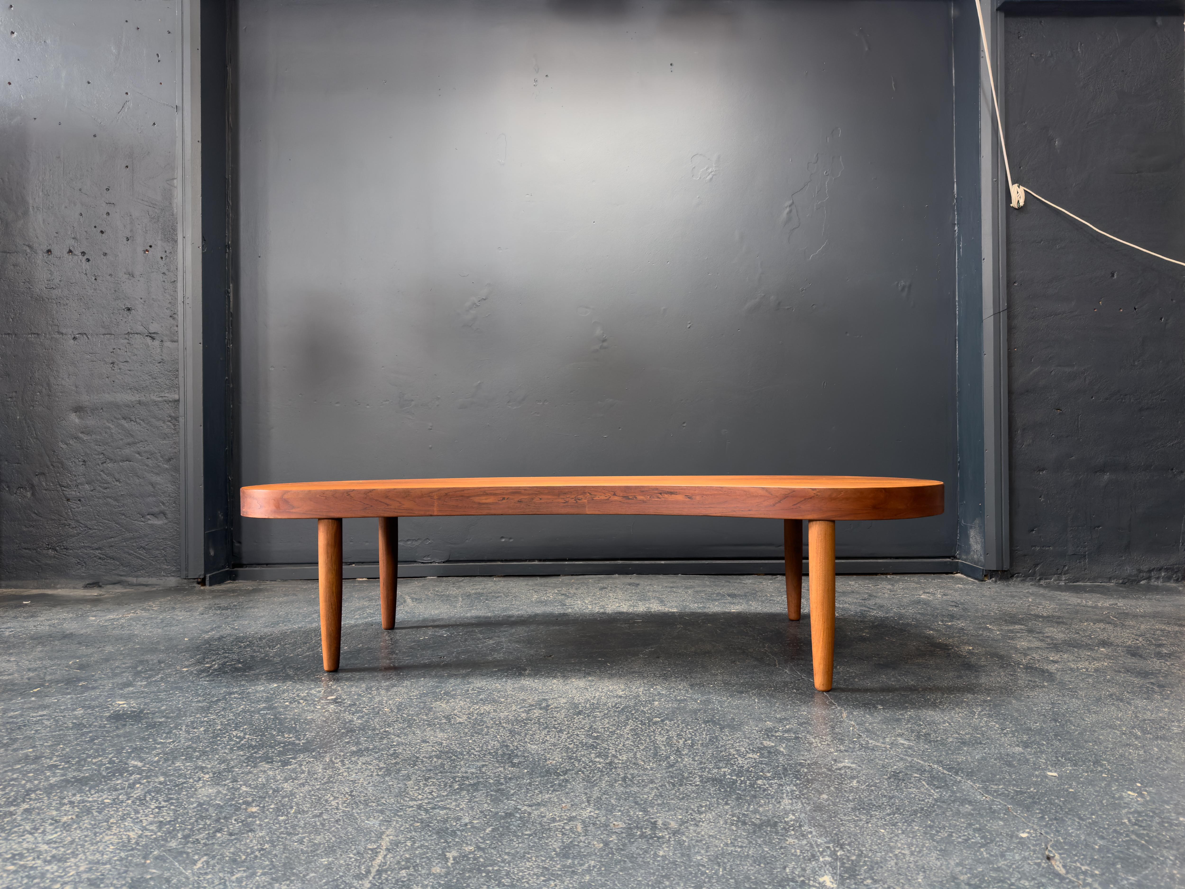 This elegant mid-century modern coffee table features a distinctive organic kidney-shaped design, embodying the natural forms and simplicity that defined the era. Crafted from solid teak, the table showcases a warm, golden grain and a beautifully