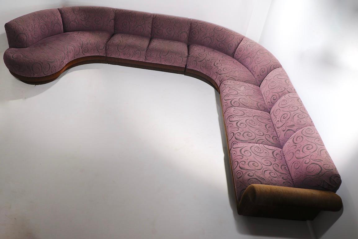 Dramatisches und beeindruckendes Sektionssofa von Weiman in luxuriösem violettem Stoff, mit zweistufigem Sockel in Brauntönen und Armlehnen. . Die Sitzgruppe besteht aus vier Teilen, zwei geraden, dem geschwungenen Teil - dem sogenannten Pie - und