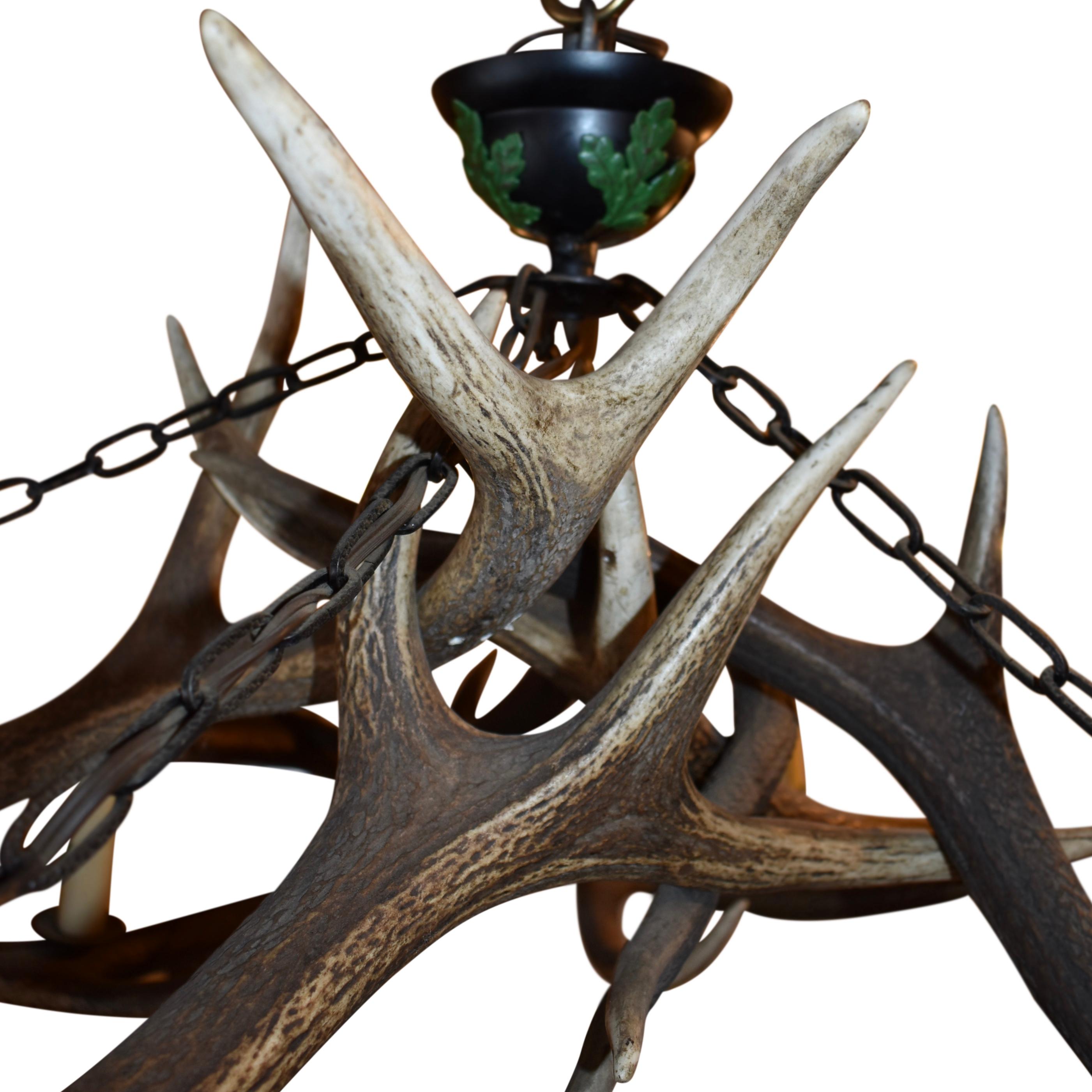 Custom made from nine red stag antlers, this beautiful chandelier features five candleholders and five faux candles. The candle holders extending from the coronets of the five outer antlers. Decorative green leaves on the faux candles and black