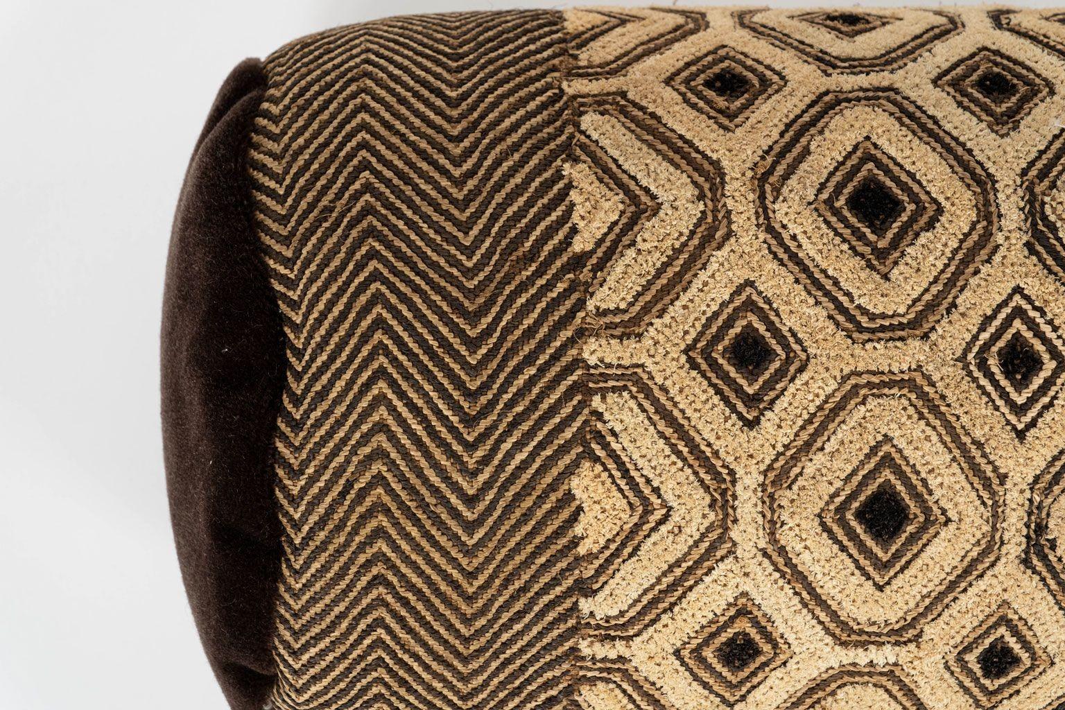 Large custom bolster cushion from vintage African Kuba cloth. Hand-dyed raphia palm handwoven in a geometric pattern in various shades of brown and gold. Dark brown wool mohair velvet comprises ends of bolster. Includes zip fastener and feather
