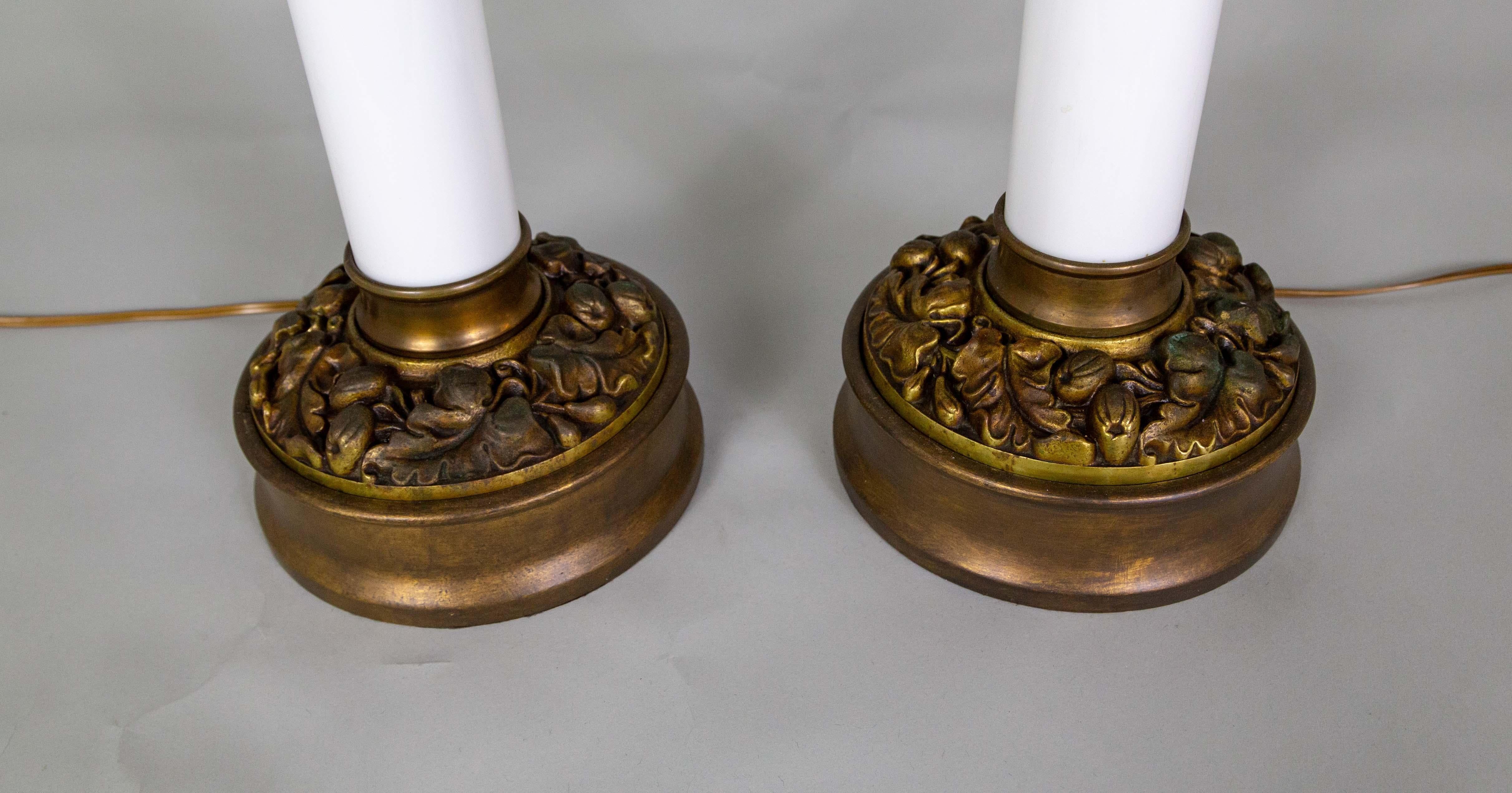 A striking pair of sizable table lamps with milk glass columns on bronze-tinted grape leaf bases. They are made by Paul Hanson Lighting Company, which operated in New York from the 1920s to the 1970s. Their high quality and design make them popular
