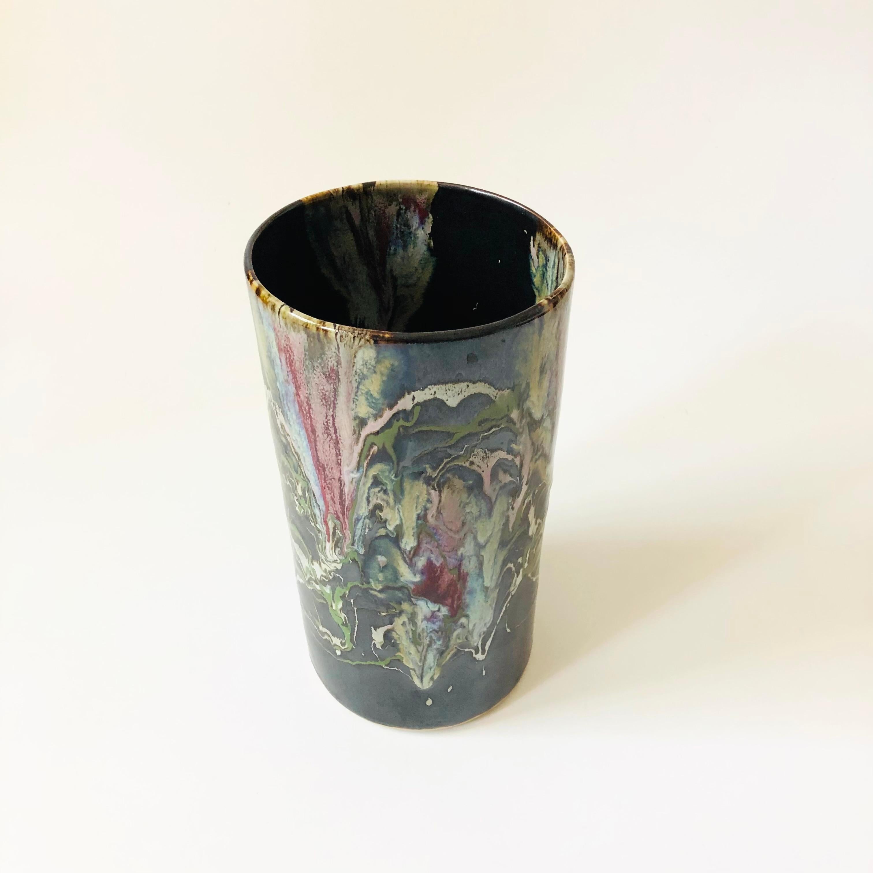 A large vintage pottery vase with a drip glaze finish. Dark base glaze color and colorful irregular drip pattern decorating the surface. Versatile cylinder shape and a slightly irregular form the hand made process.

