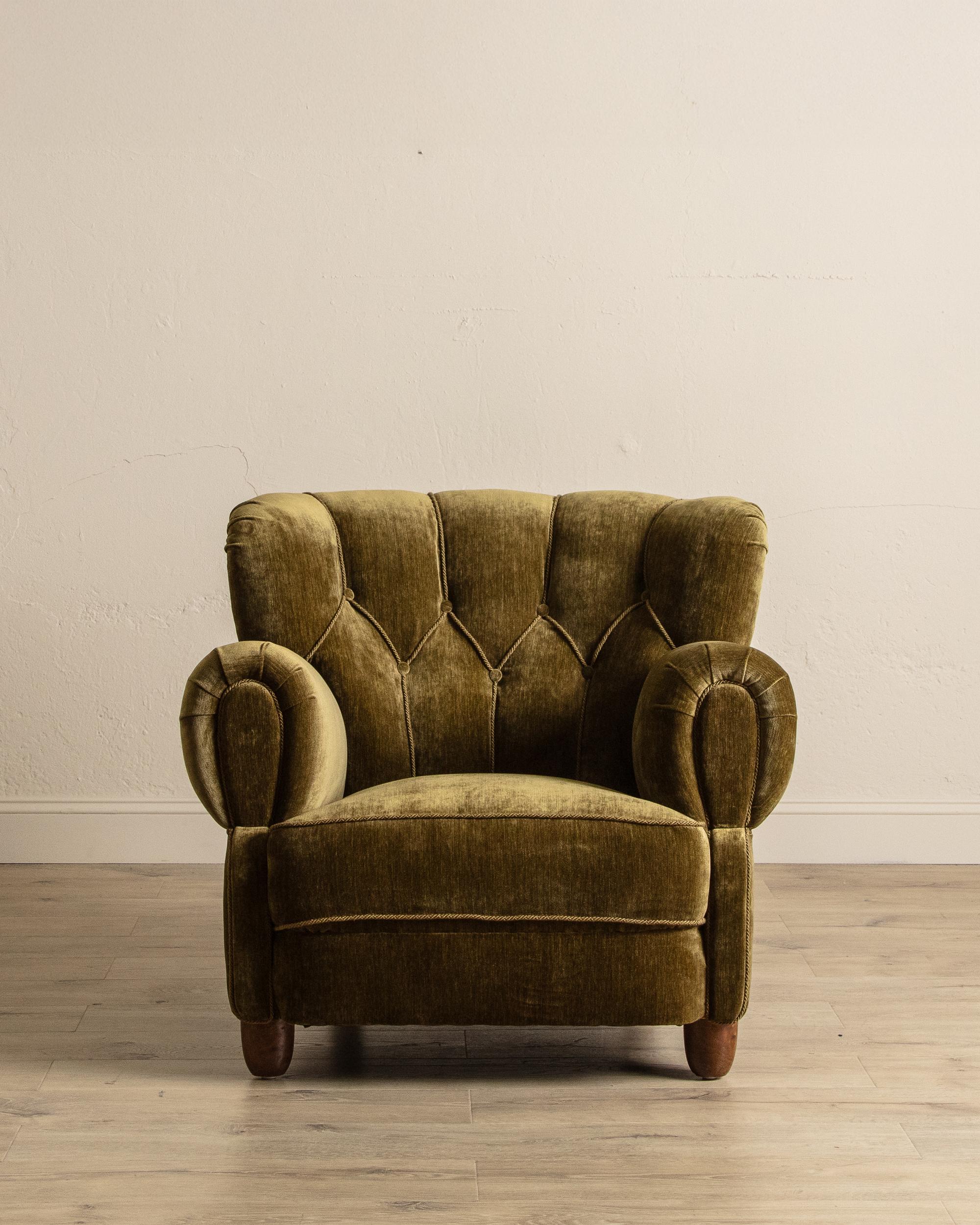 This large Danish club chair from the 1940s showcases mid-century charm through its generously curved silhouette and luxurious presence. Professionally restored and reupholstered in a soft marled olive-green velvet with coordinating rope trim, it