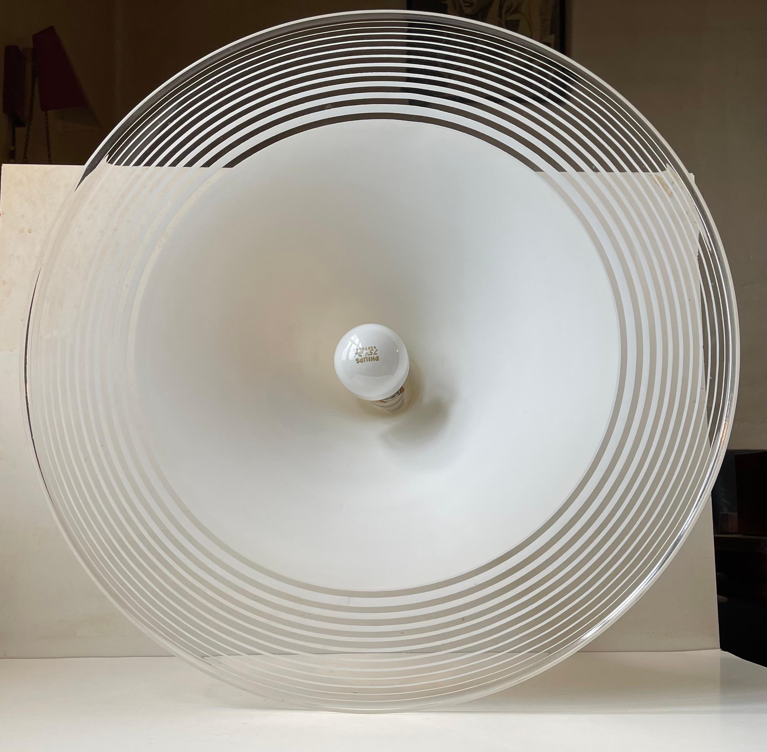 Un gran platillo volante colgante (52 cm de diámetro) de acrílico rayado blanco y transparente. Tiene un bello aspecto ingrávido gracias a sus líneas orgánicas y a la delicada composición de sus colores. Una elección brillante y natural para tu mesa