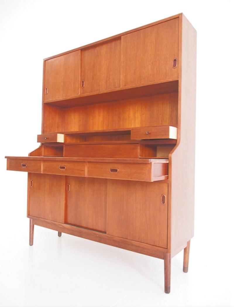 Veneered teak cabinet, buffet or secretary. Front top: three doors behind which are shelves and pullout trays. Bottom: small drawers, pullout writing table and three sliding doors. Round tapered oak legs. Restored, some drawers move a bit tightly.