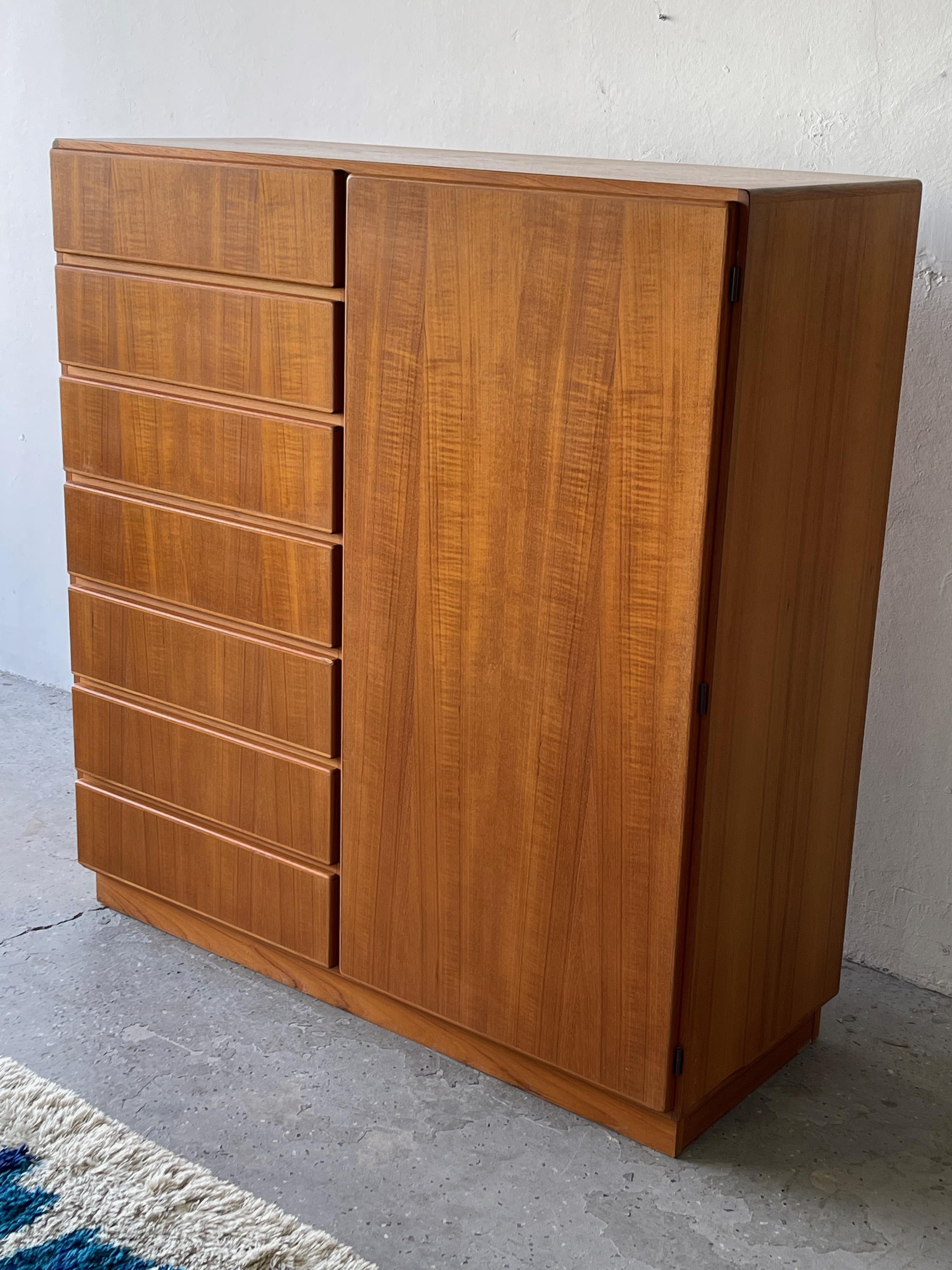 This Mid-Century Modern, minimalist Large Danish teak highboy dresser/ gentleman’s chest features a column of 7 deep drawers on the left side and a cabinet door on the right, opens to reveal 3 adjustable shelves and 2 interior drawers , offering