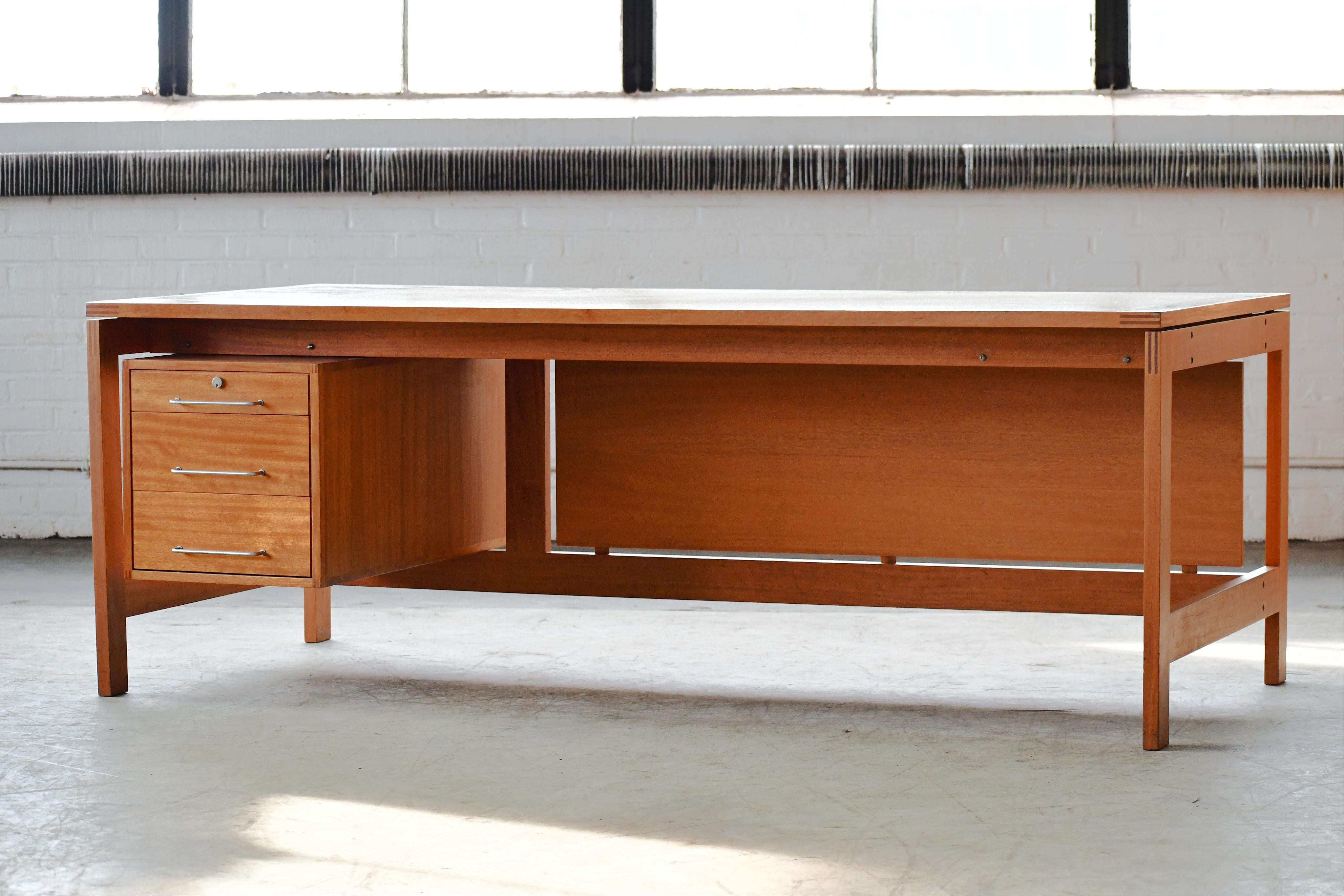Very attractive large writing desk designed by Henning Jensen & Torben Valeur circa 1970 as model M40 for Munch Møbler, Denmark. High quality solid build in a beautiful light mahogany with contrasting edges and metal pulls. Sharp precise design